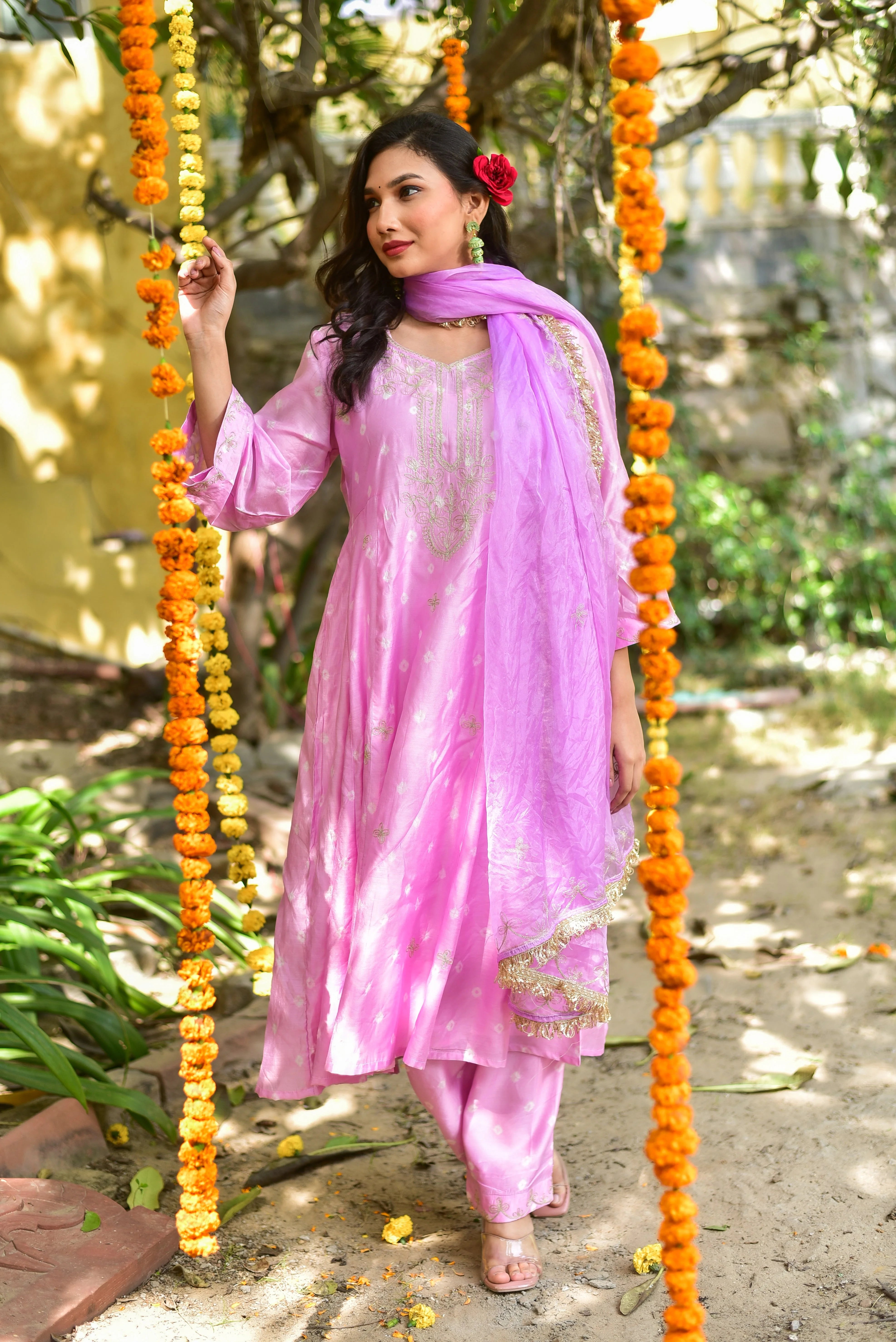 Woman in a pink traditional outfit sitting on a swing decorated with orange flowers.