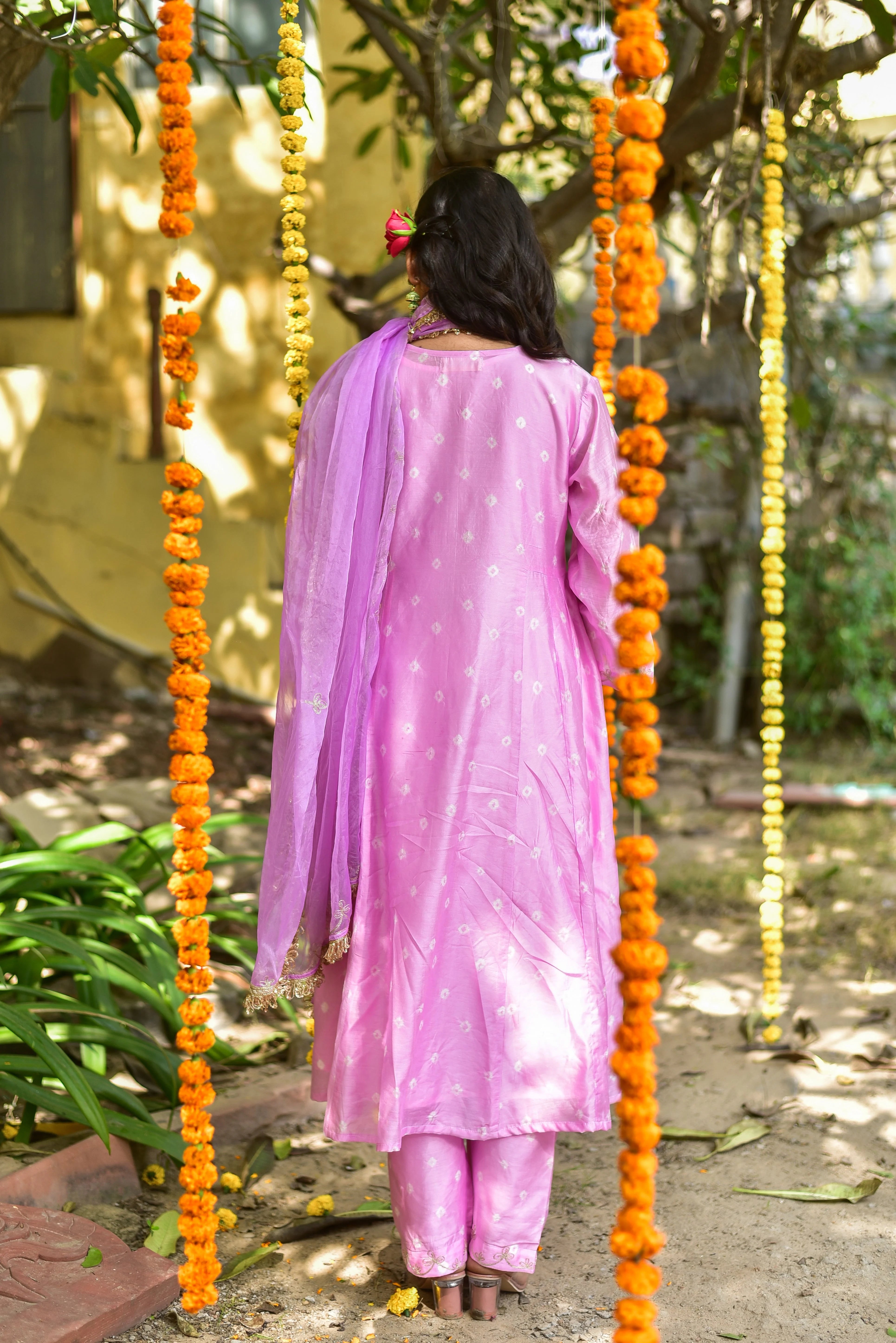The image depicts a woman in traditional Indian attire, showcasing a stunning pink salwar kameez with intricate Mukesh work. The outfit is crafted from luxurious silk fabric, featuring a long kurta with a round neckline and three-quarter sleeves, paired with matching pants and a dupatta adorned with delicate tassels.
The vibrant pink hue is complemented by subtle gold accents, adding a touch of sophistication to the overall design. The Mukesh work, a traditional Indian embroidery technique, is skillfully w