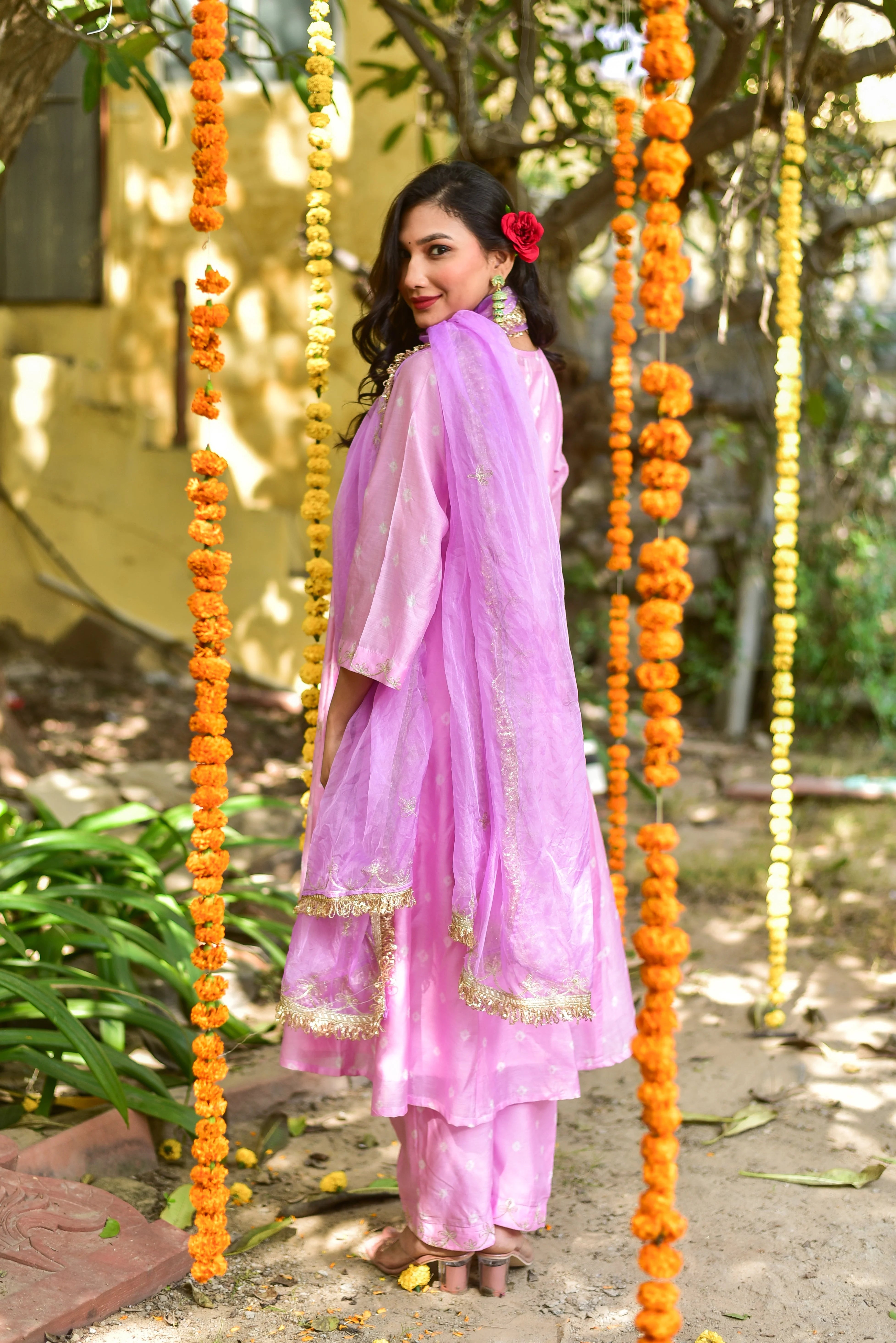 The image showcases a woman dressed in a stunning pink salwar kameez, a traditional Indian outfit. The ensemble consists of a long tunic, wide-legged pants, and a matching dupatta, all crafted from a lightweight, sheer fabric with a subtle gold pattern. The outfit is further embellished with intricate gold embroidery along the edges of the tunic and dupatta, adding an extra touch of elegance.
The woman's attire is complemented by her long, dark hair, which cascades down