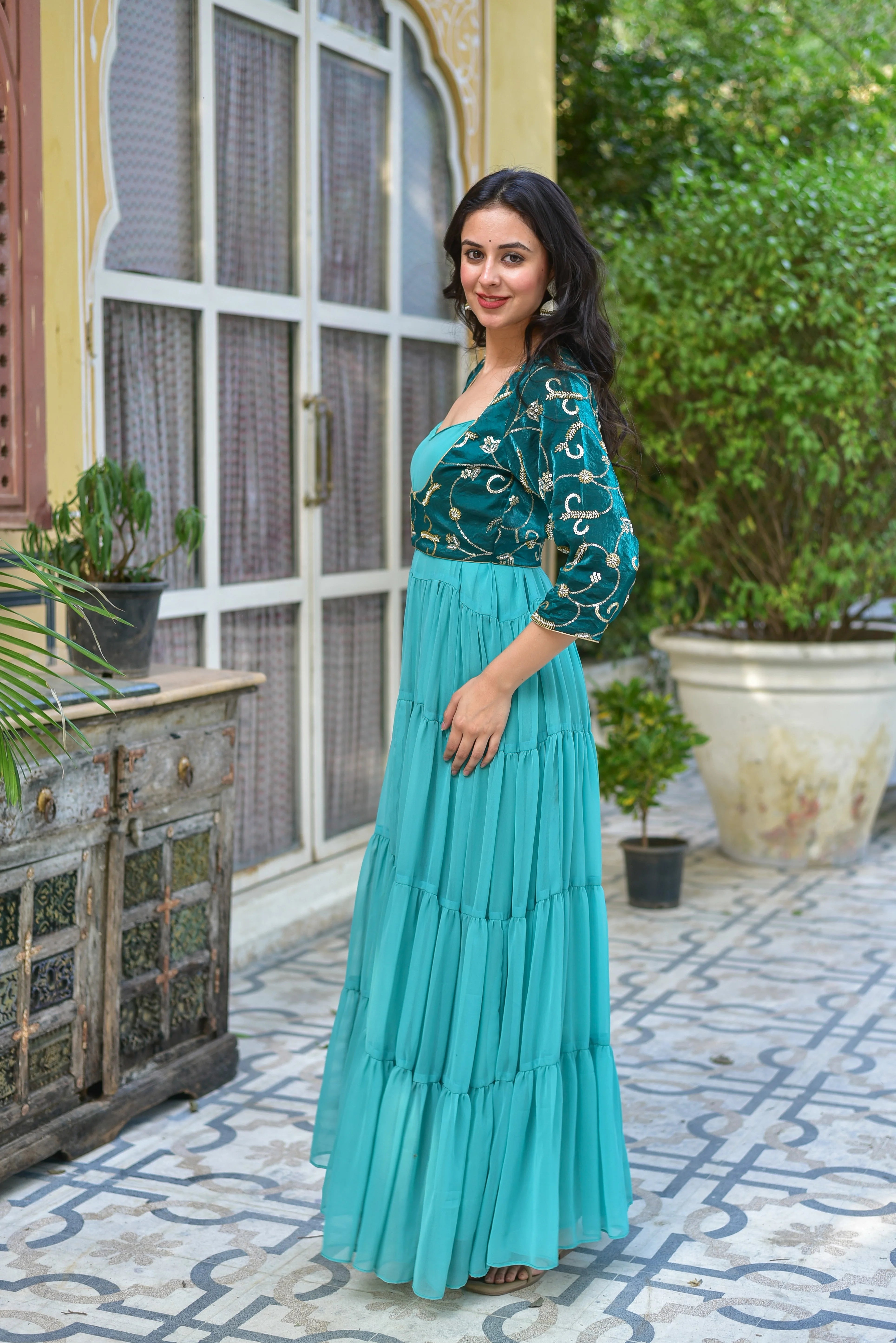 The image showcases a woman modeling a stunning green tiered dress with a matching jacket, exuding elegance and sophistication. The dress features a flowing georgette fabric and a beautiful tiered design that creates a graceful silhouette. The jacket is adorned with intricate embroidery, adding a touch of traditional craftsmanship to the overall look.
The woman's long black hair and elegant pose complete the image, making it perfect for a fashion or lifestyle magazine.