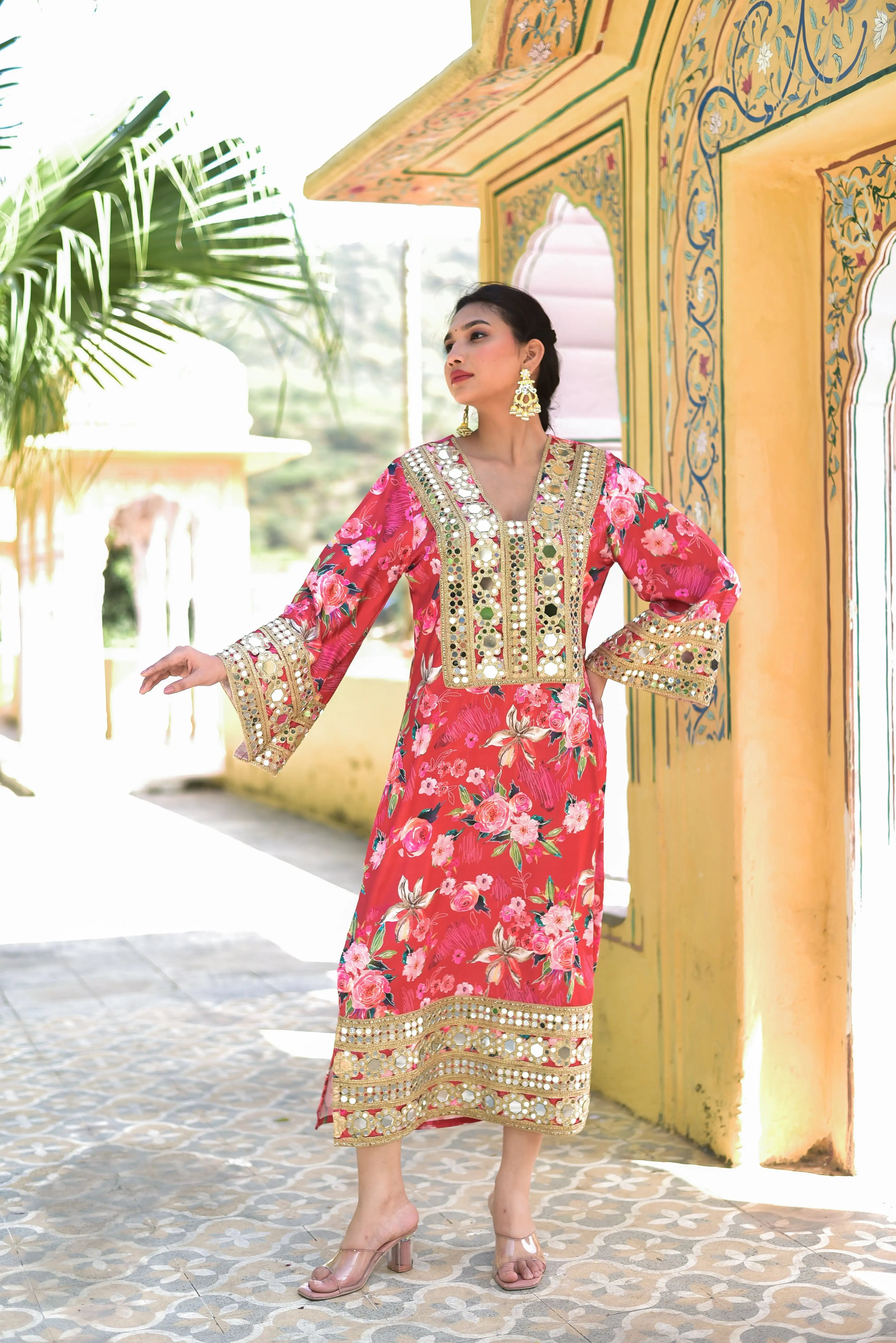 The image showcases a woman wearing a stunning floral-printed, long-sleeved dress with a V-neckline and mirror embellishments, exuding elegance and sophistication. The dress features a vibrant floral print on a luxurious satin fabric, complemented by mirror work that adds a touch of glamour. The woman's confident pose and the dress's elegant design make for a captivating visual. This product is perfect for those seeking a stylish and eye-catching addition to their wardrobe.