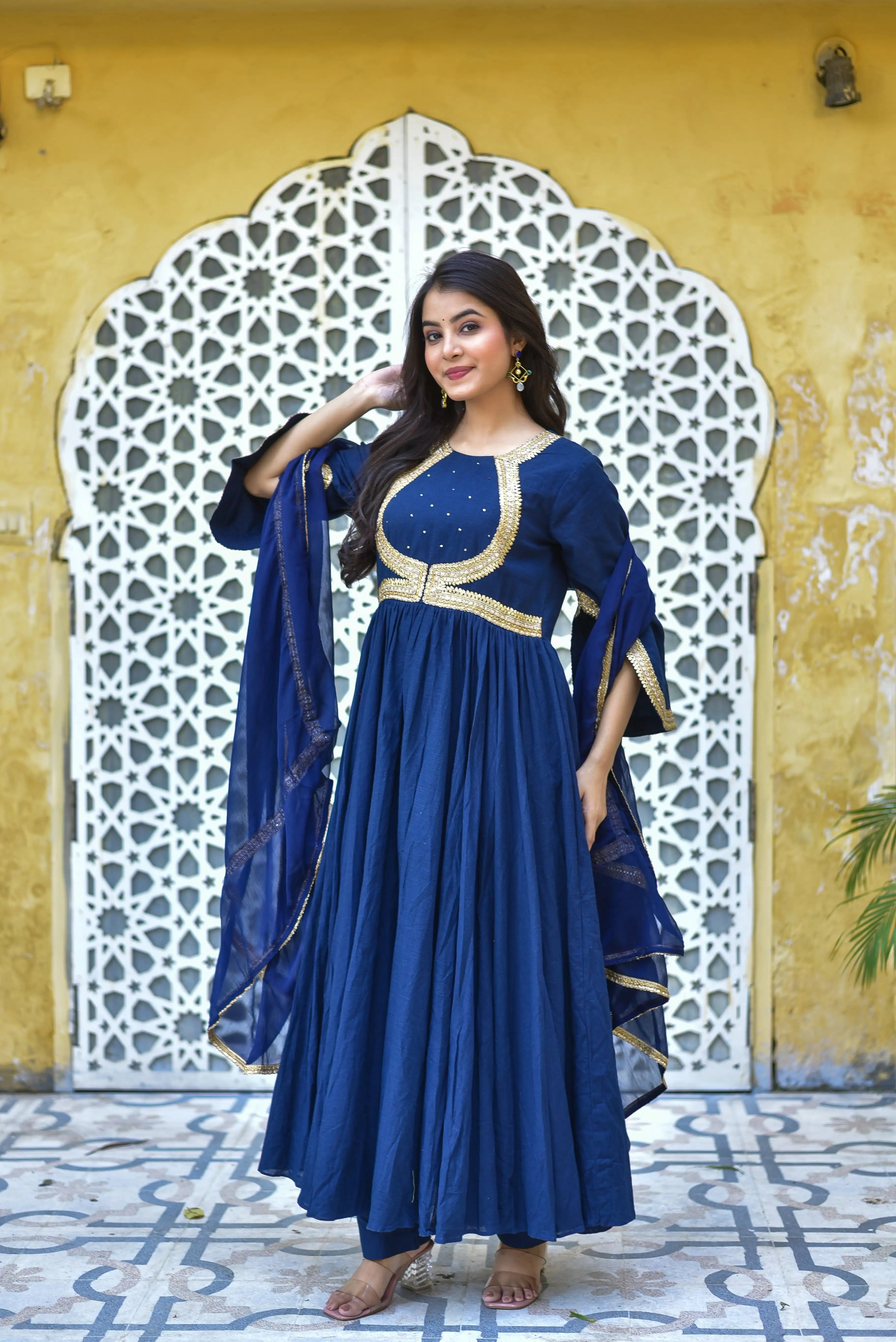The image depicts a woman in a stunning blue dress, exuding elegance and sophistication. The dress is a deep shade of blue, complemented by gold accents that add a touch of luxury. The fabric appears to be a lightweight material, possibly silk or chiffon, which drapes elegantly on the woman's body.
The dress features a classic design with a round neckline and a flowing skirt that falls just above the ankles. The sleeves are long and flowy, adding to the overall sense of drama