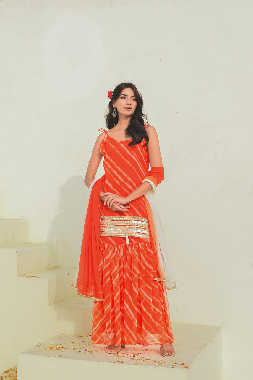 Woman in a red saree with white patterns standing on a staircase.