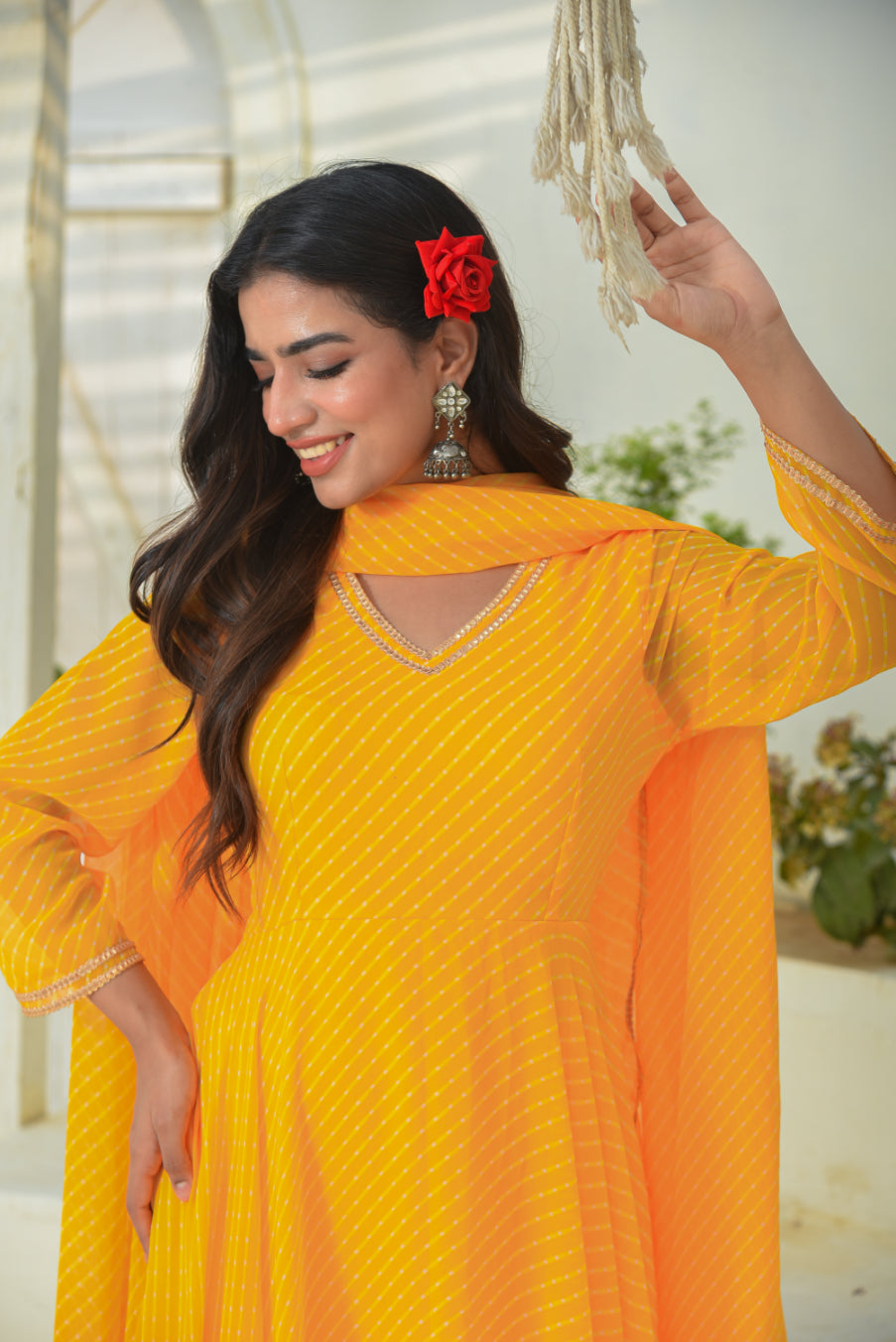 Woman wearing a bright yellow outfit with a red flower in her hair, standing indoors.