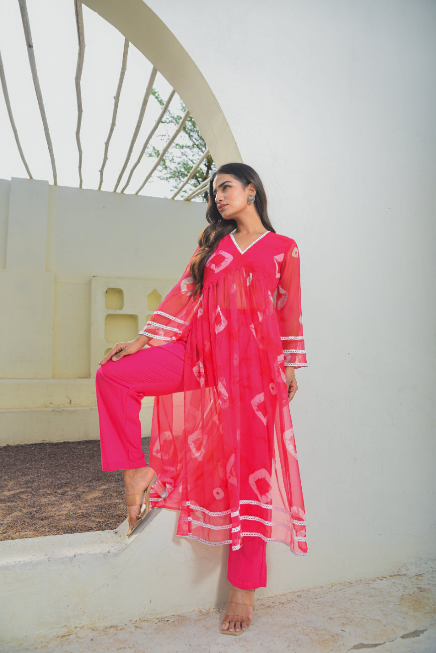 Woman in a bright pink traditional outfit standing against a white wall.