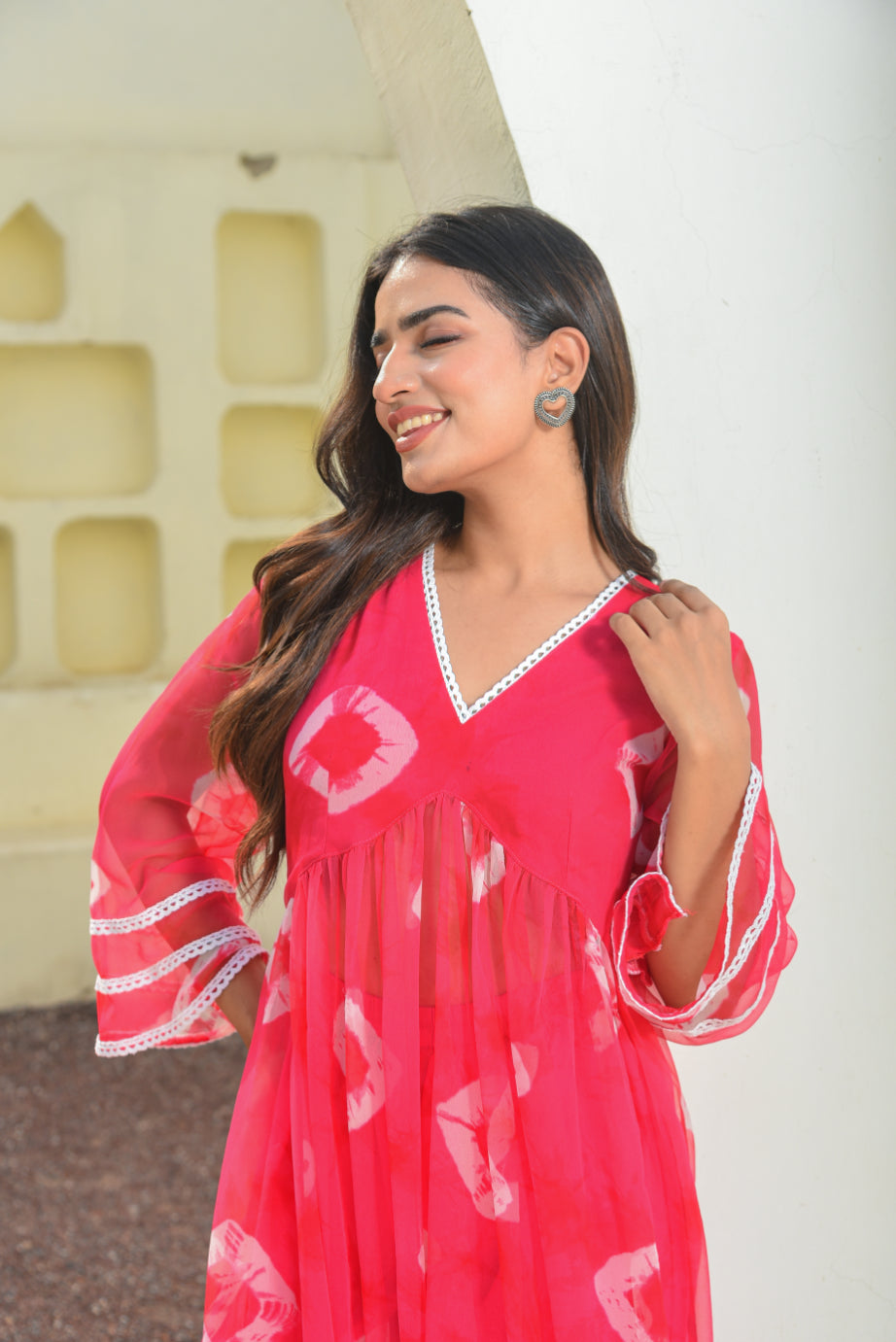 Woman wearing a red dress with white patterns against a light-colored wall.
