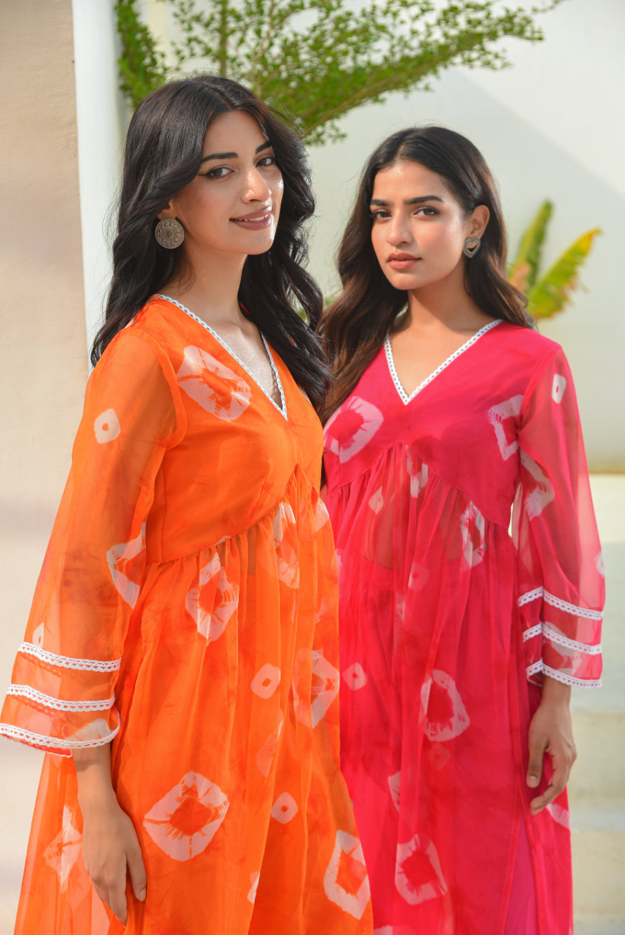Two women wearing orange and pink dresses with white patterns, standing outdoors.