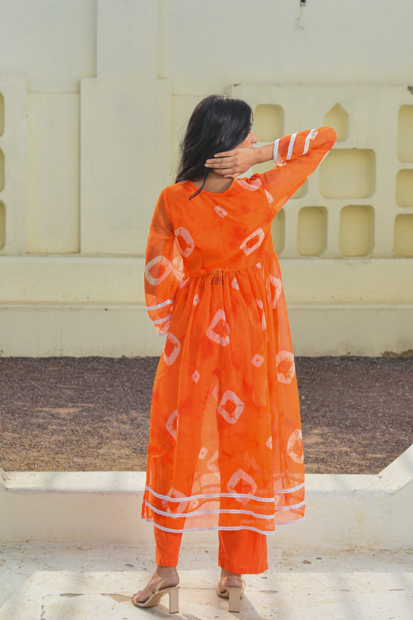 Person wearing an orange dress with white patterns, standing against a light-colored wall.