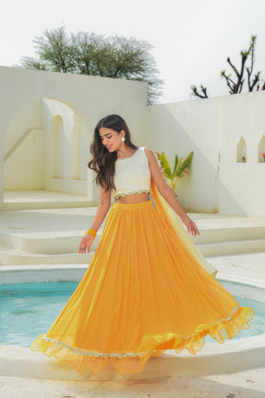 Woman in a yellow and white traditional outfit standing in a serene outdoor setting.