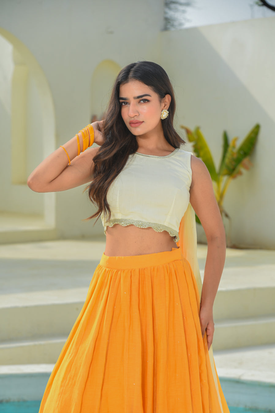 Woman in a light green top and orange skirt standing by a pool with a neutral background