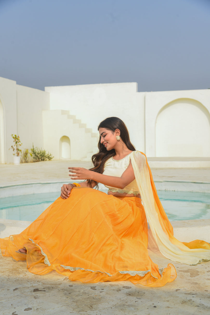 Woman in a yellow and white saree sitting by a pool with a white architectural background