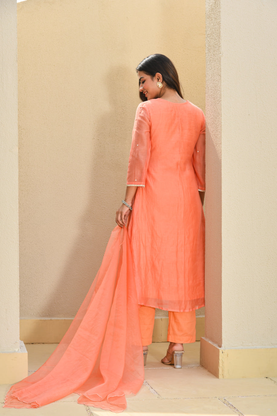 Woman wearing a peach-colored traditional outfit with a dupatta in an indoor setting.