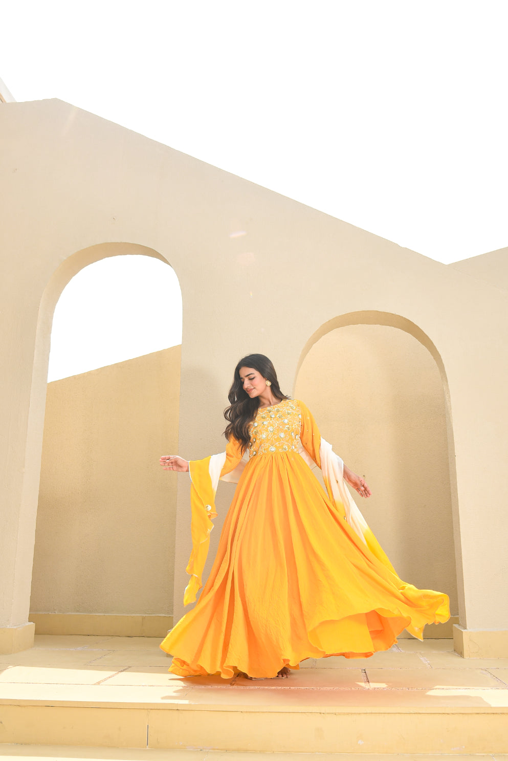 Woman in a yellow dress standing in front of beige architectural arches.