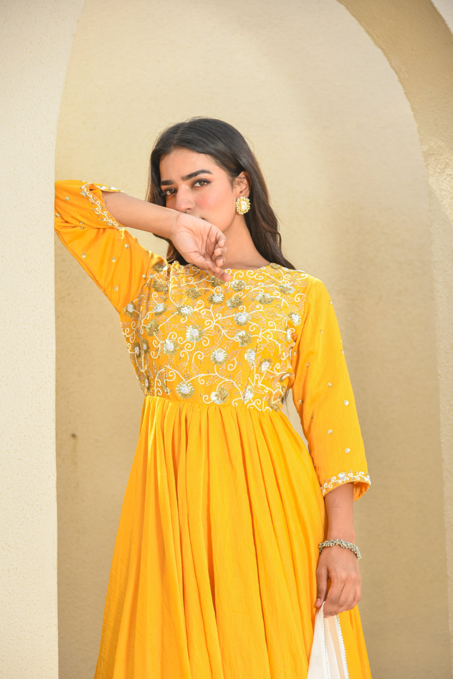 Woman wearing a yellow dress with intricate designs against a beige background