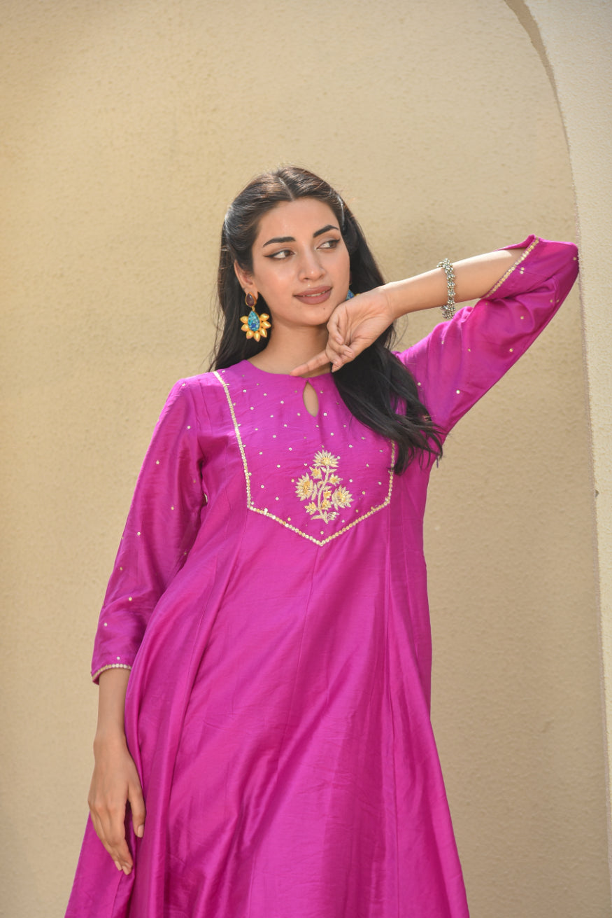Woman wearing a pink traditional outfit with floral embroidery against a beige background