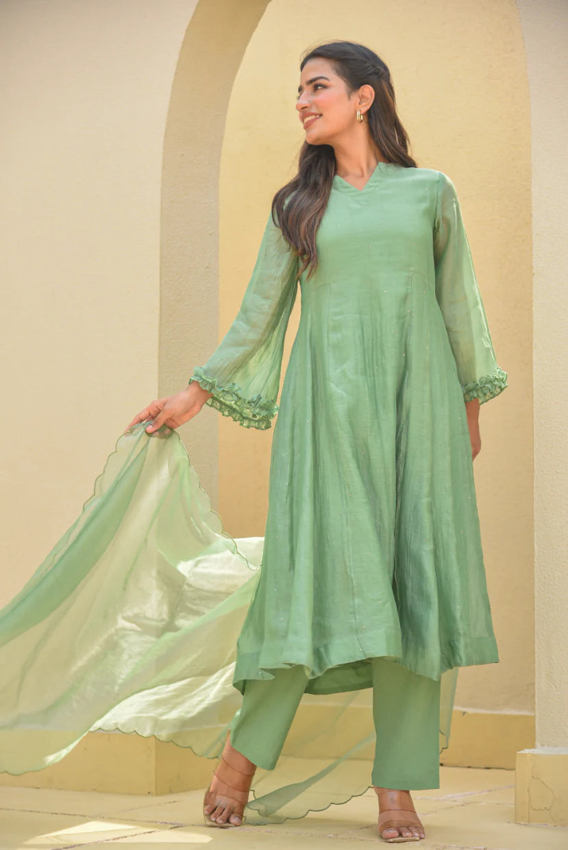 The Mukesh Work A-line Kurta Set by Asya by Saroj Jain is a stunning ensemble that exudes elegance and sophistication. Crafted from premium Mal Chanderi, this set features an exquisite A-line kurta adorned with delicate, hand-crafted Mukesh work that catches the light beautifully. The kurta's A-line silhouette creates a flattering fit, while the scalloped edges add a touch of whimsy. The matching pants and dupatta complete the look, making it perfect for any occasion.