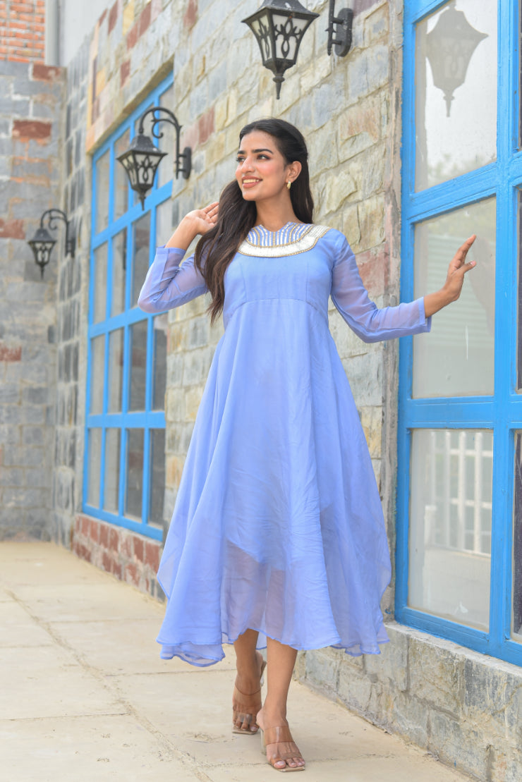 Woman in a light blue dress standing in front of a building with blue-framed windows.