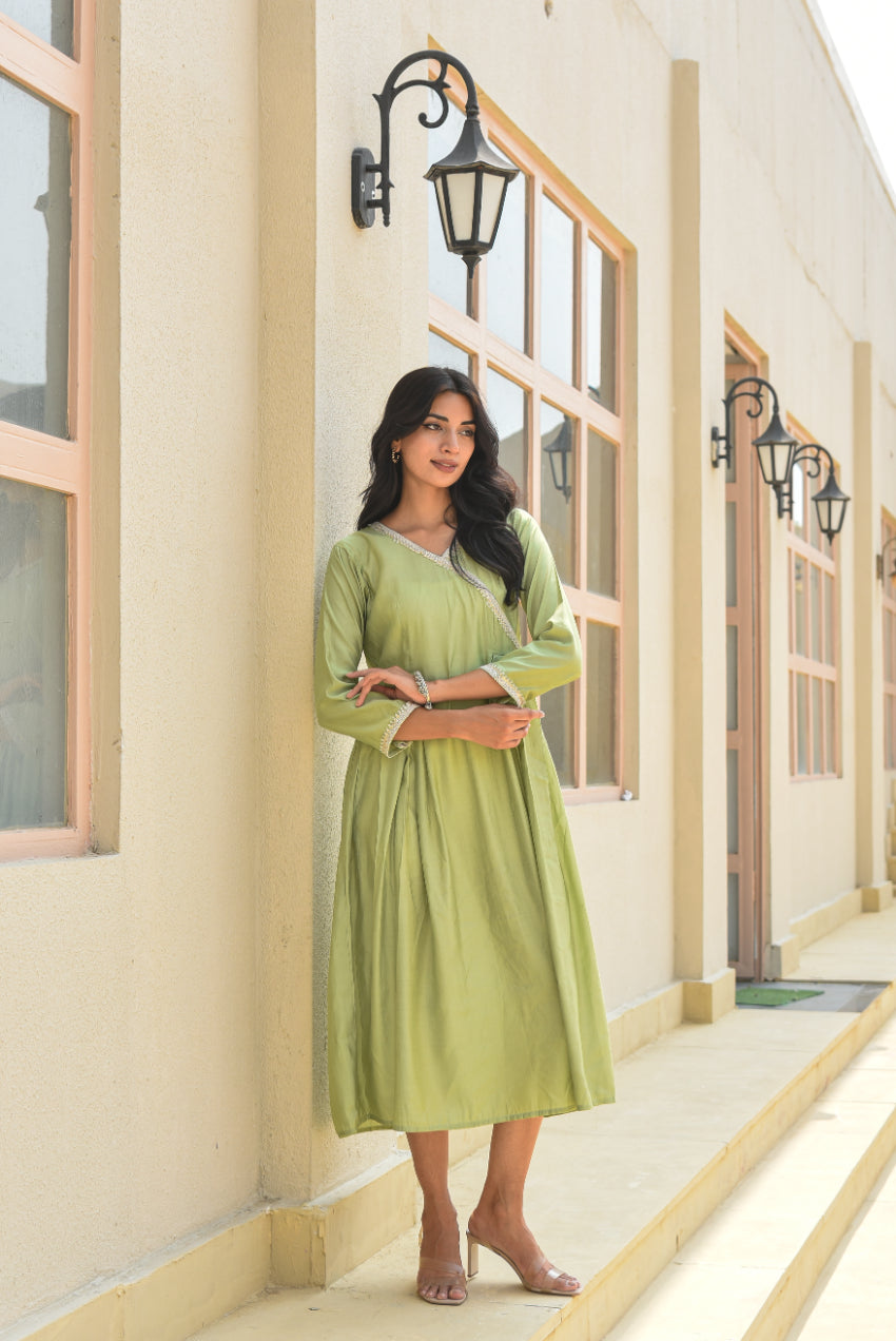 Woman in a green dress standing against a building with large windows.