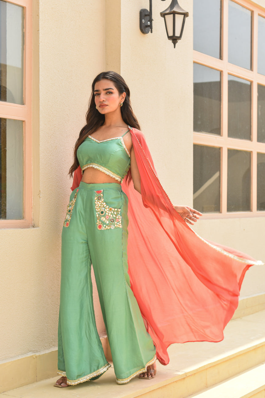 Woman in green traditional outfit with pink dupatta standing outdoors.