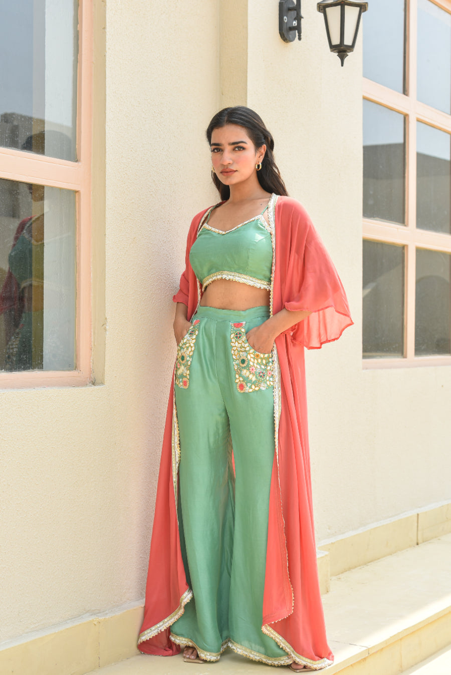 Woman in a green traditional outfit with a pink dupatta standing in front of a building.