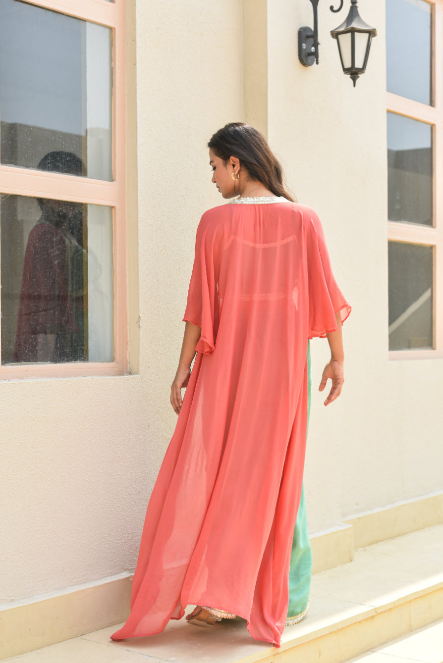 Woman wearing a coral dress standing in front of a building with large windows.