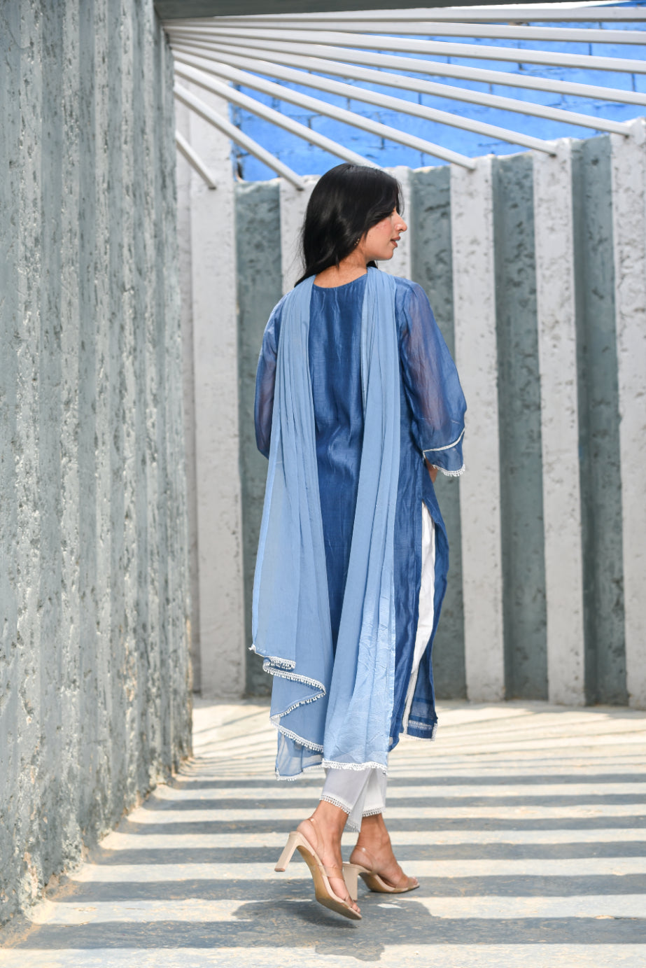 Woman in a blue outfit walking on a sunlit path with geometric patterns.