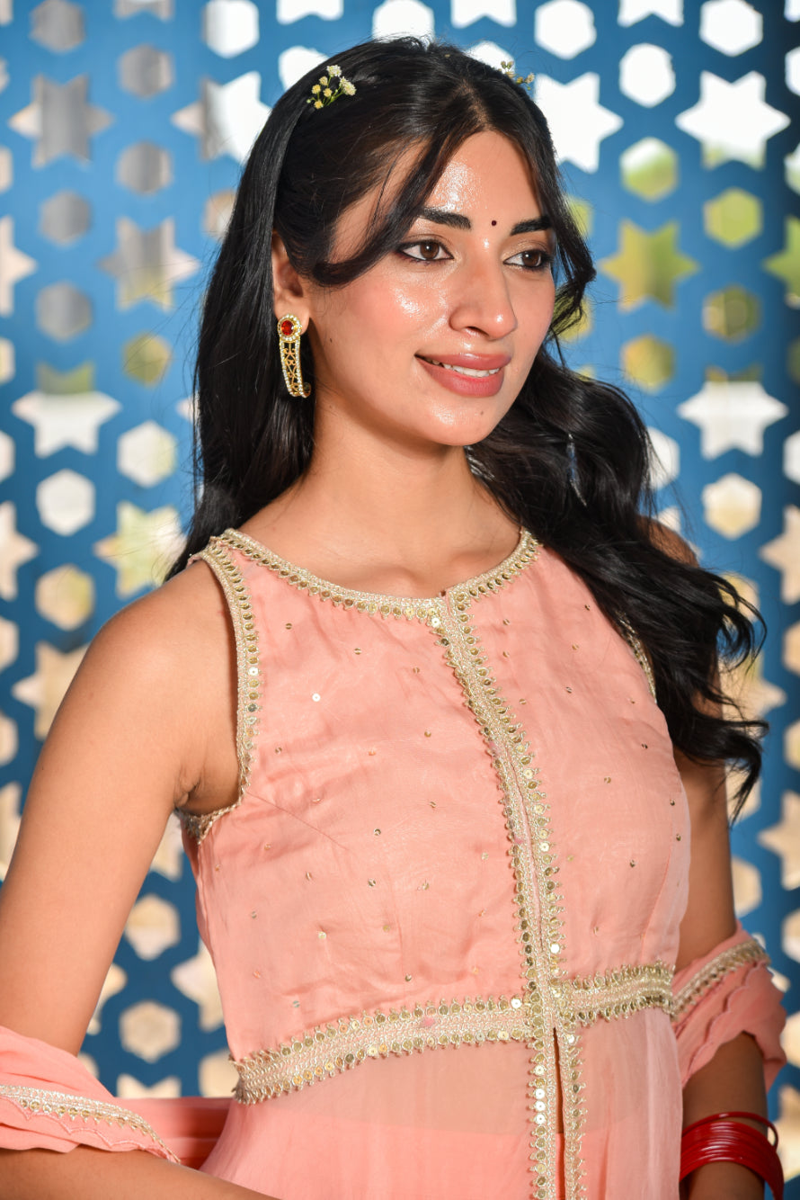 Woman wearing a pink traditional outfit with gold details against a decorative blue and white background