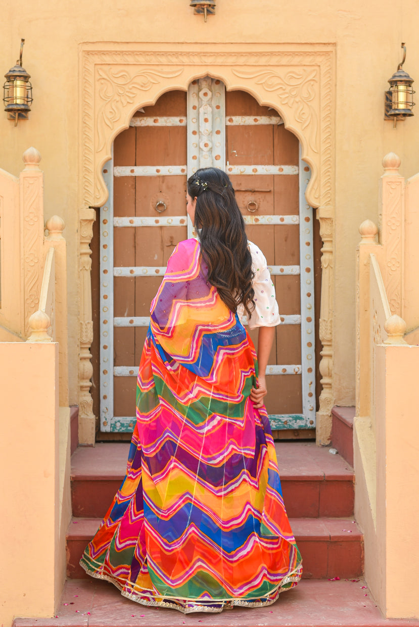 Woman in a colorful traditional dress standing in front of an ornate wooden door.
