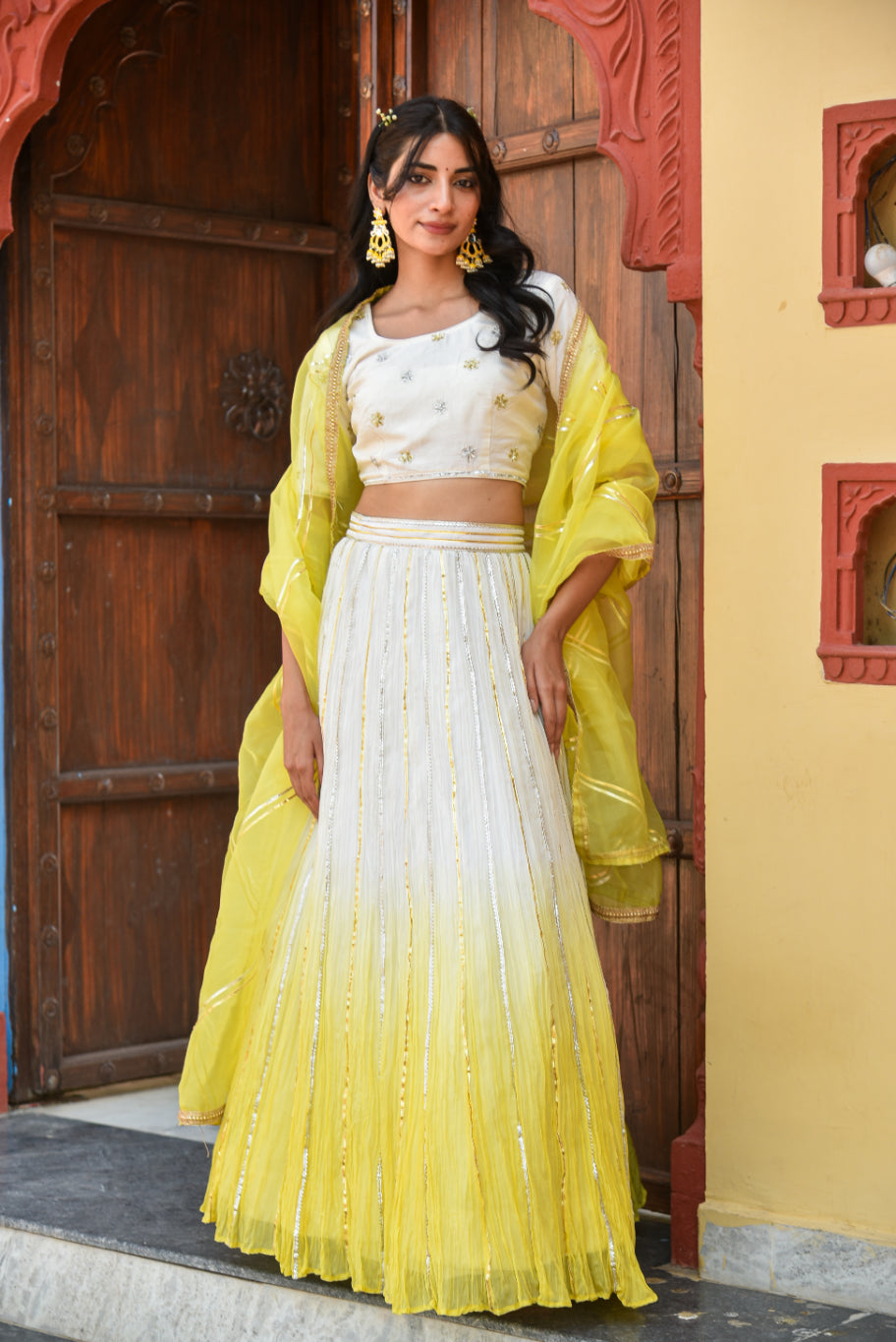 Woman in a yellow and white traditional outfit standing in front of a wooden door.