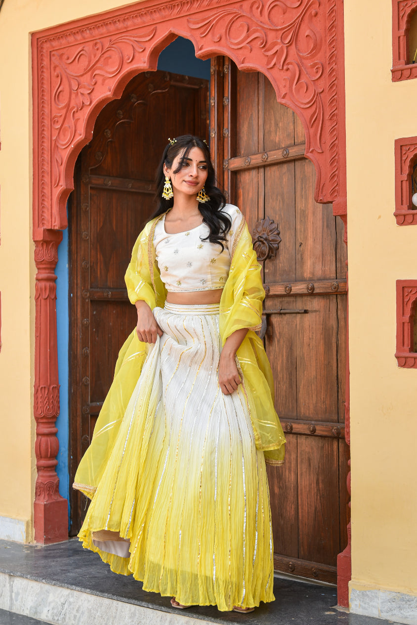 Woman in a yellow and white traditional outfit standing in front of a decorative wooden door.