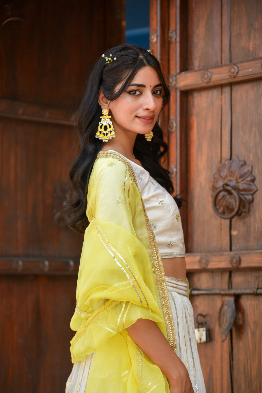 Woman in a yellow saree standing in front of a wooden door.