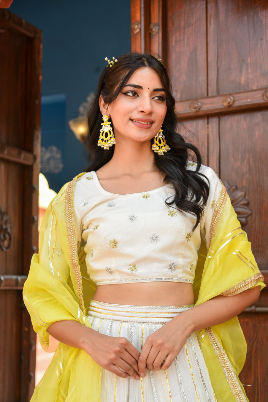 Woman in a yellow and white traditional outfit standing in front of a wooden door.