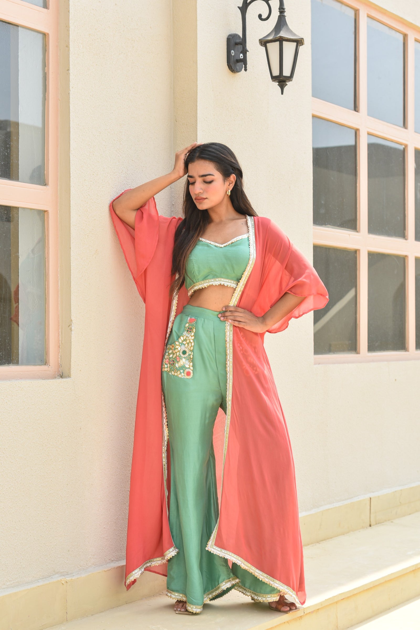 Woman in a green outfit with a pink duster standing against a building.
