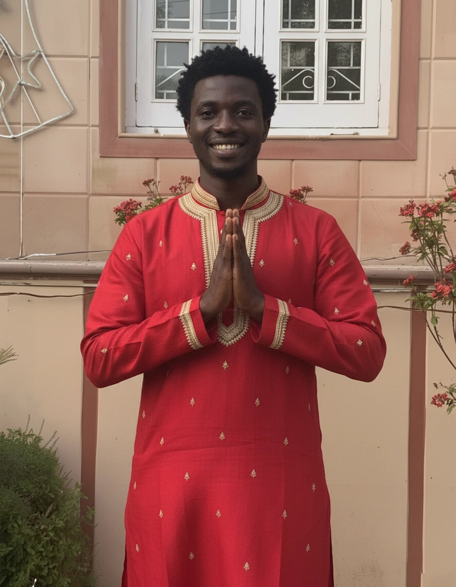 Man in a red traditional outfit standing in front of a window with floral decorations.