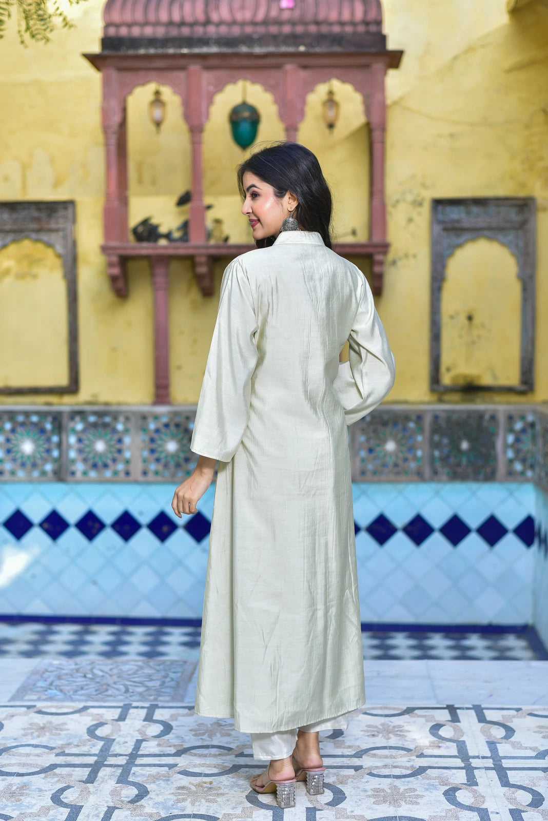 The Creamy Kaju Katli Pleated Kurta Set is a stunning 2-piece ensemble that exudes luxurious elegance. The set features a creamy white kurta with intricate pleating details, paired with matching pants. The fabric appears to be a soft, lightweight material, likely cotton or silk, which drapes elegantly on the body. The kurta's high neckline and long sleeves add a touch of sophistication, while the pleated design creates a beautiful, flowing silhouette.