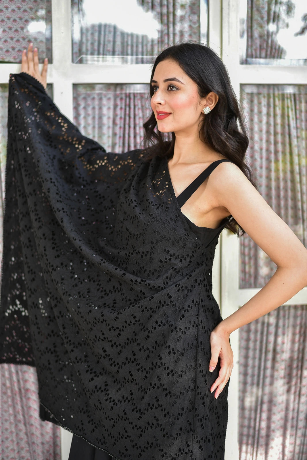 The image features a woman wearing a stunning black saree, exuding elegance and sophistication. The saree is crafted from intricate black lace fabric, adorned with delicate floral patterns that add a touch of femininity and charm. The fabric appears to be made of a lightweight material, such as silk or chiffon, which drapes elegantly around her body.
The woman's attire is complemented by a matching black blouse, featuring a V-neckline and thin straps that add a touch of modesty and