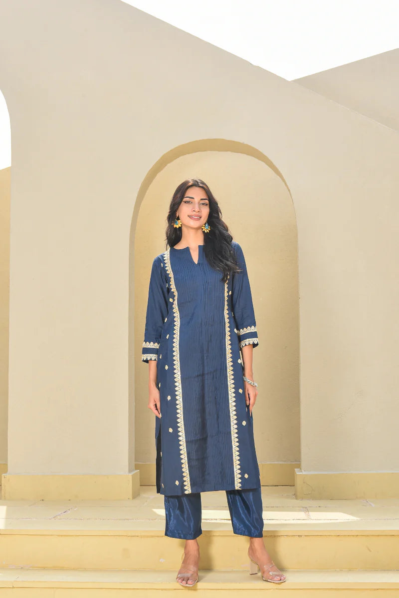 This navy blue set features a kurta with a slit neckline and 3/4 sleeves, crafted from rich Pollyn silk with elegant zari work. Paired with a comfortable cotton pant featuring a half-elastic waist and pull-up kurta closure, it offers a perfect blend of style and comfort for festive or semi-formal occasions.
