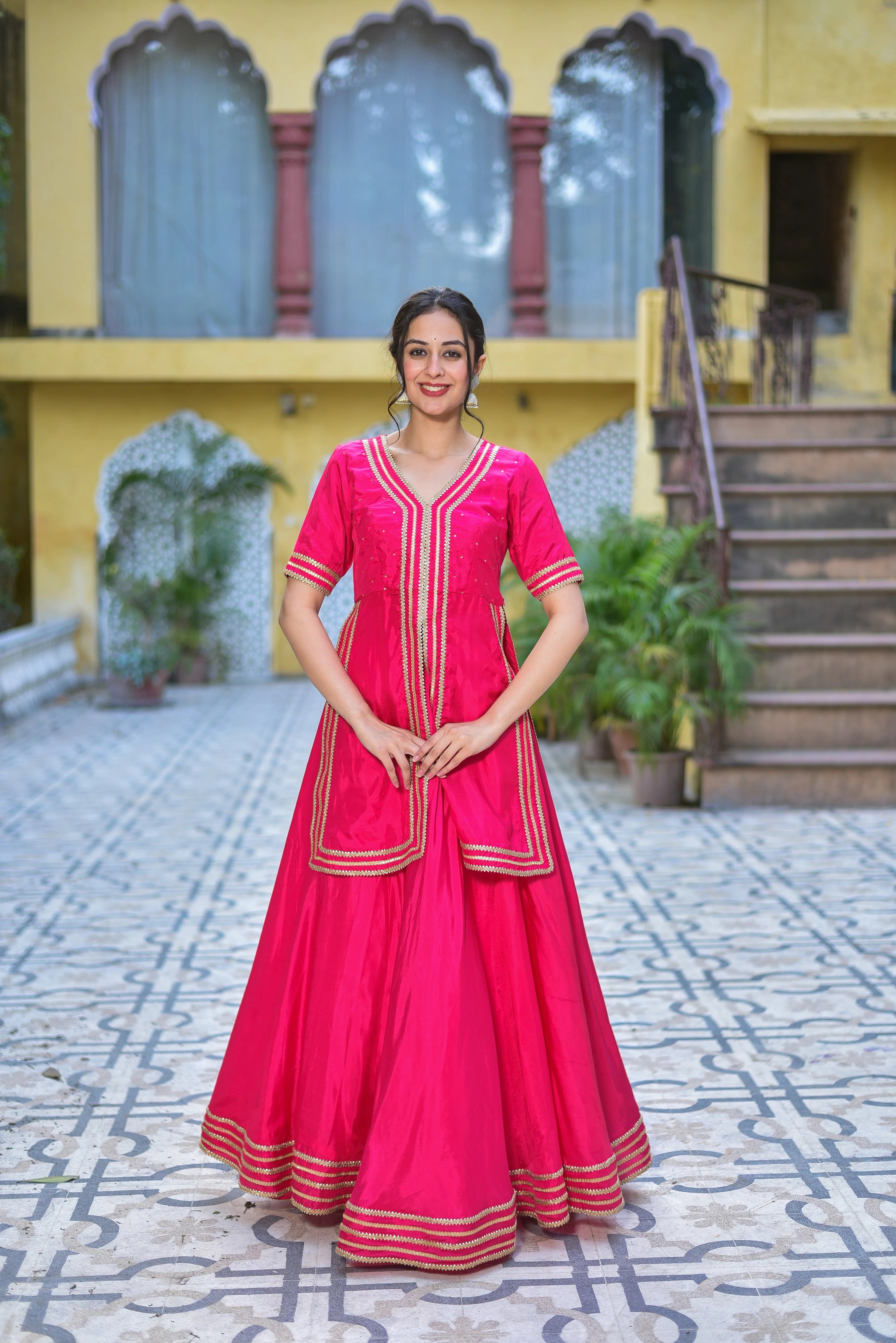 The Pink Rani sa indo-western set is a stunning fusion of traditional elegance and contemporary fashion, crafted from luxurious silk blend fabric that drapes beautifully and feels incredibly soft against the skin. This exquisite ensemble features a V-neckline and elbow-length sleeves, adorned with intricate gota detailing that adds a touch of sophistication. The full skirt is a showstopper, with a flared silhouette and a striking border that complements the gota detailing perfectly.