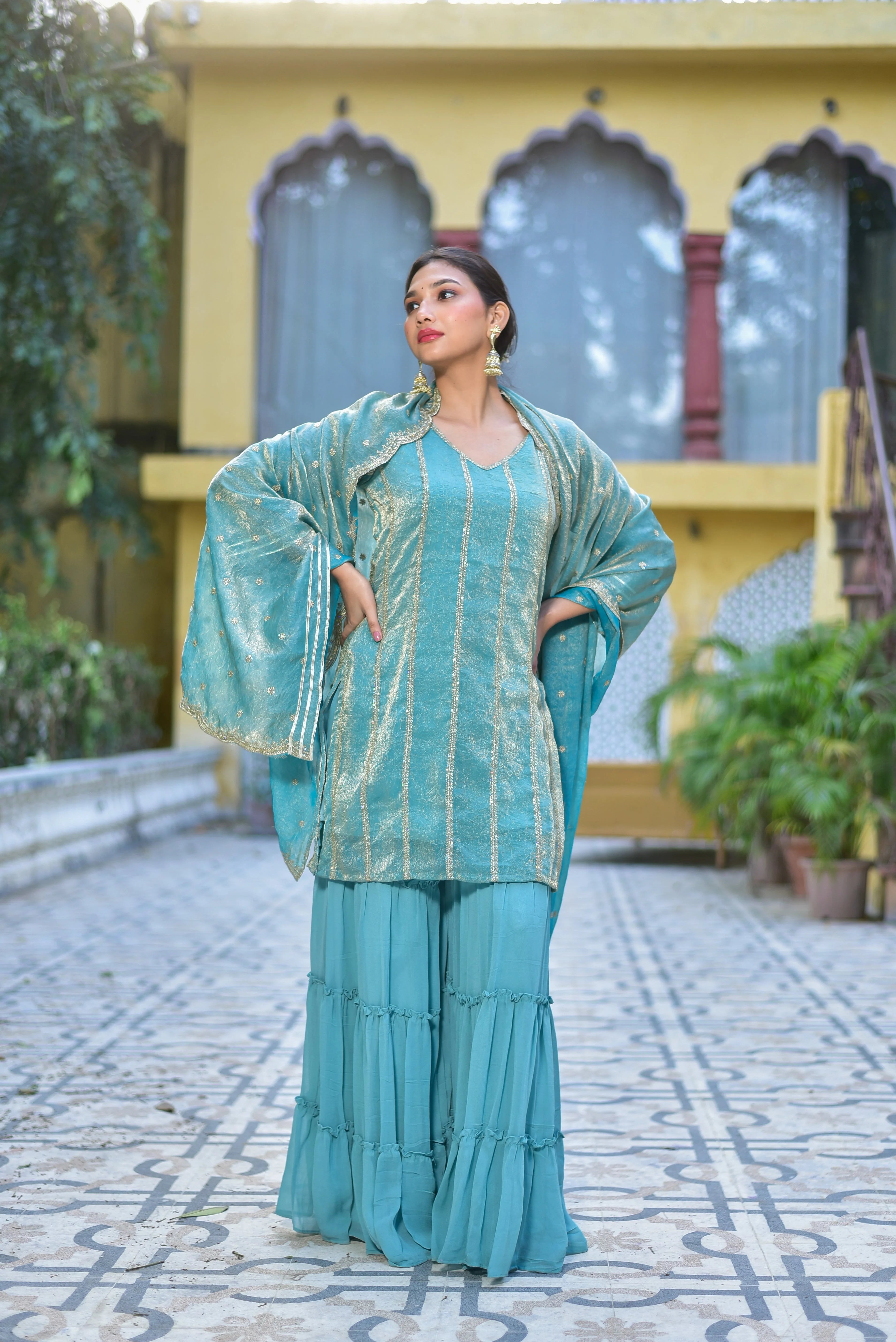 The Sea Green Kurta Sharara Set is a stunning ensemble that exudes elegance and sophistication. Crafted from high-quality fabric, this set features a sea green kurta with intricate gold embroidery, complemented by a matching sharara and a beautiful dupatta. The kurta boasts a V-neckline and long sleeves, while the sharara has a tiered design that adds volume and movement to the overall silhouette. The dupatta is adorned with delicate gold embroidery, adding a touch of luxury to the outfit.