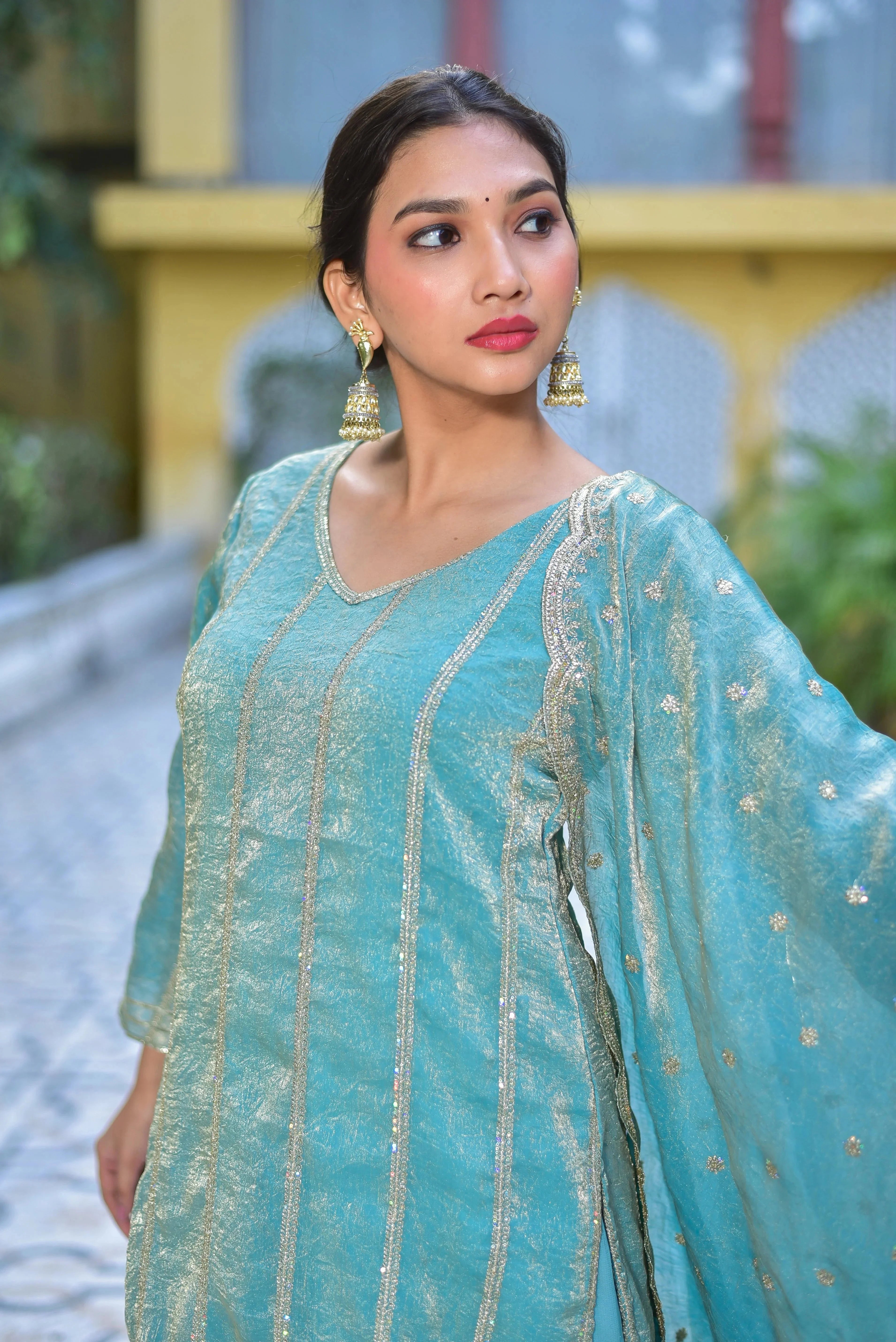 This Sea Green Kurta Sharara Set is a stunning ensemble that exudes elegance and sophistication. The sea green hue, reminiscent of a tranquil ocean, sets the tone for a refined and cultured look. Crafted from luxurious fabric, the kurta boasts intricate gold embroidery, adding a touch of opulence to the overall design. The sharara pants, with their flowing silhouette, create a dramatic effect, while the matching dupatta completes the set with a sense of continuity and cohesion.