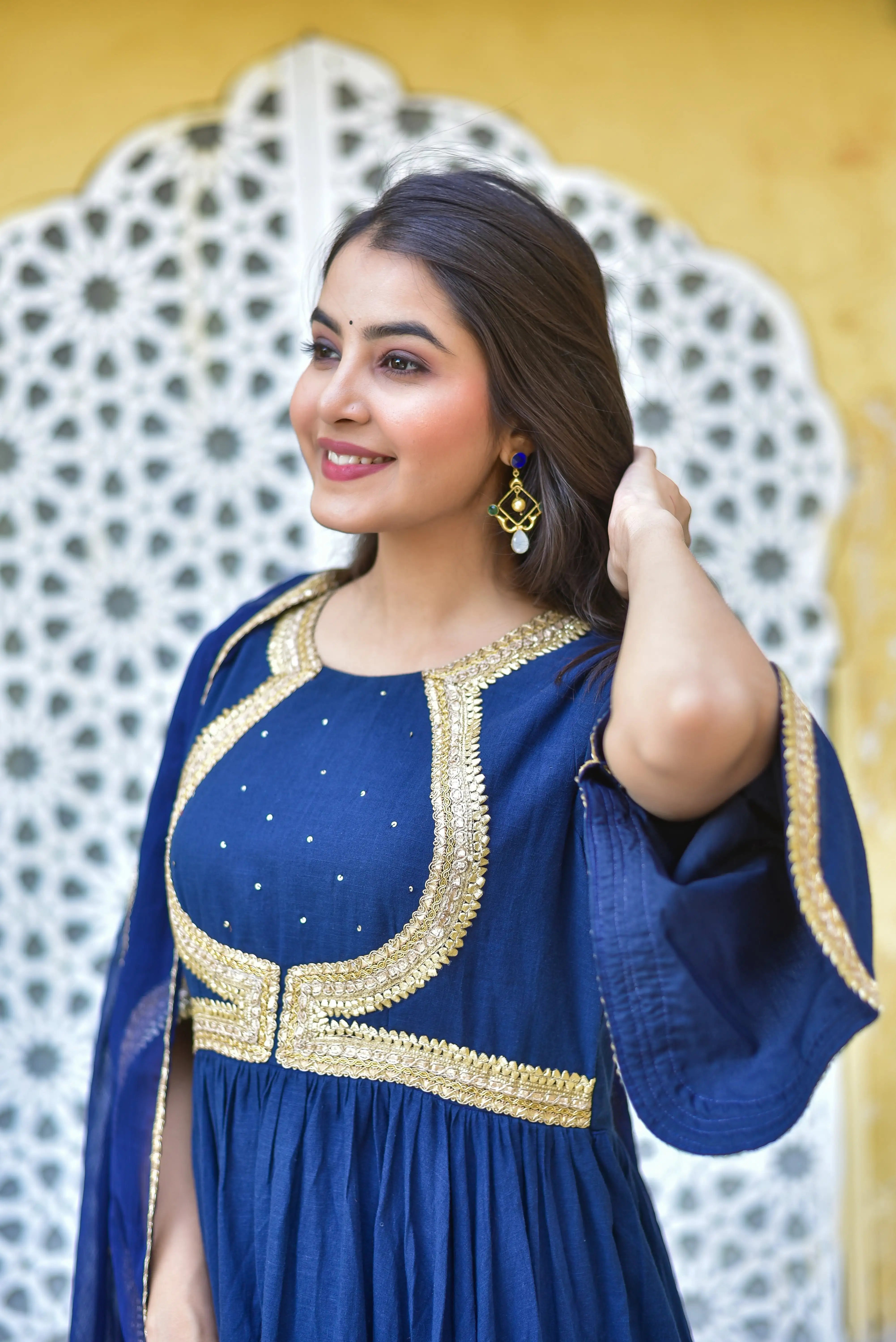 The image depicts a woman wearing a stunning blue dress with gold embroidery, exuding elegance and sophistication. The dress features a round neckline and three-quarter-length sleeves, crafted from a lightweight fabric that drapes beautifully around her body.

The blue hue is complemented by intricate gold embroidery, adding a touch of luxury to the overall design. The dress is adorned with a matching blue dupatta, which adds a pop of color and texture to the overall look.

The woman's dark hair is styled n