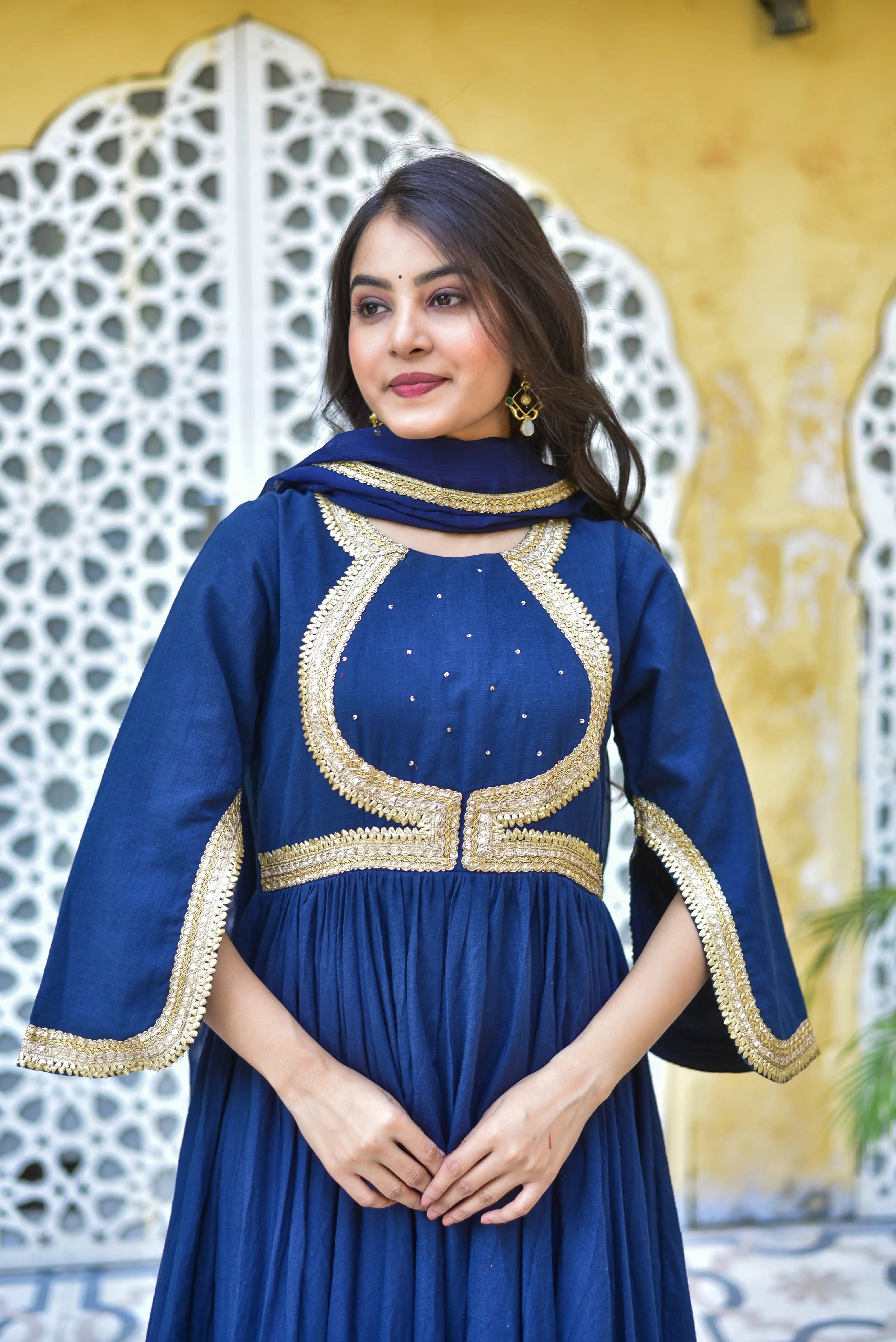The image showcases a woman wearing a stunning blue dress with intricate gold detailing, exuding elegance and sophistication. The dress features a high neckline and a flowing skirt, with a fitted bodice that cinches at the waist, creating a flattering silhouette. The gold trim adds a touch of luxury, while the flowy sleeves and matching scarf complete the outfit, creating a cohesive and stylish look.

The dress is crafted from a lightweight fabric, likely cotton or silk, and is adorned with delicate gold em