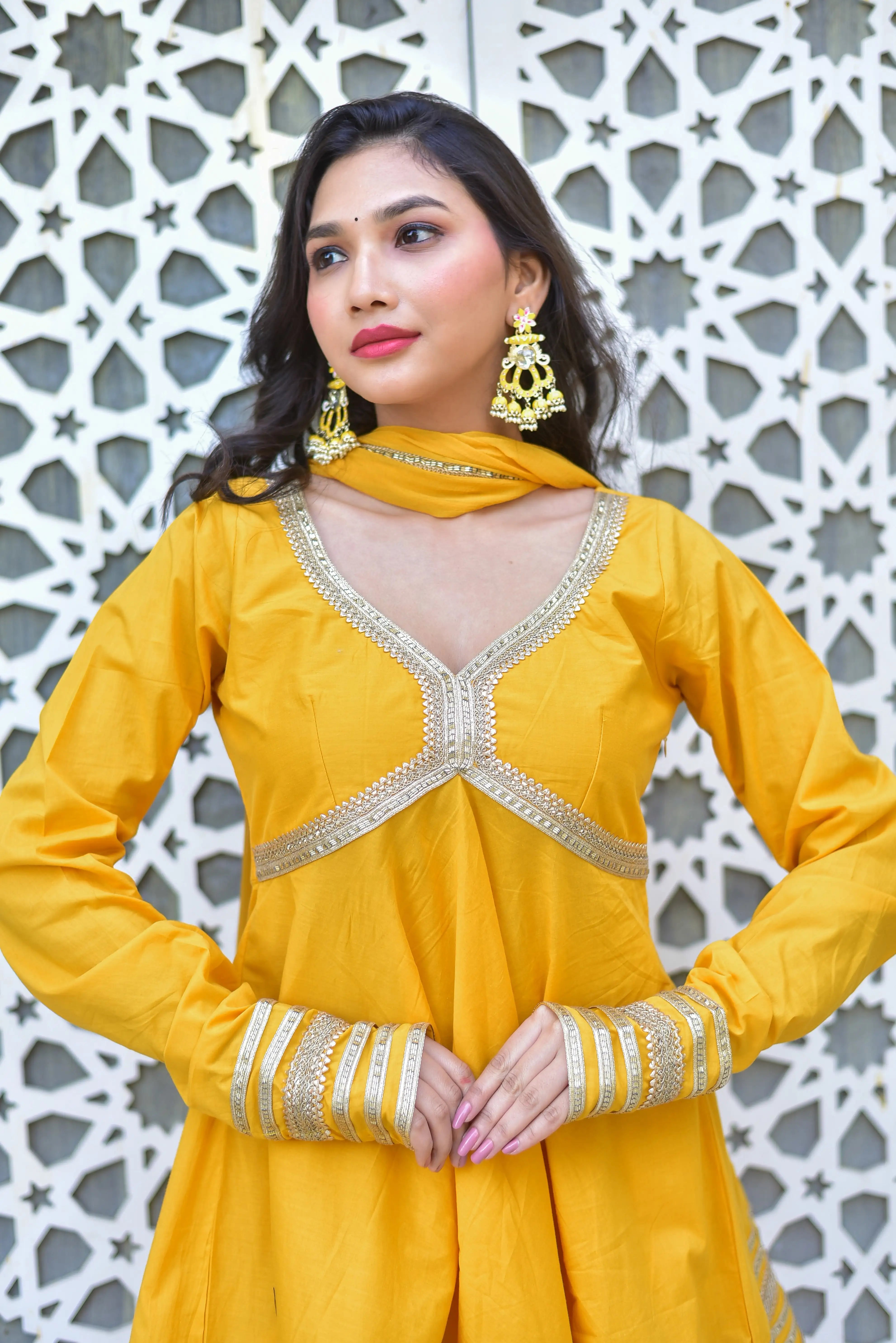 This image showcases a stunning peet amber sharara suit set, exuding warmth and elegance in its rich mustard-yellow hue. The set features intricate gold embroidery along the neckline, sleeves, and bottom of the sharara pants, adding a touch of sophistication to its overall design. The long-sleeved V-neck top and matching dupatta with gold detailing create a cohesive and stylish look.