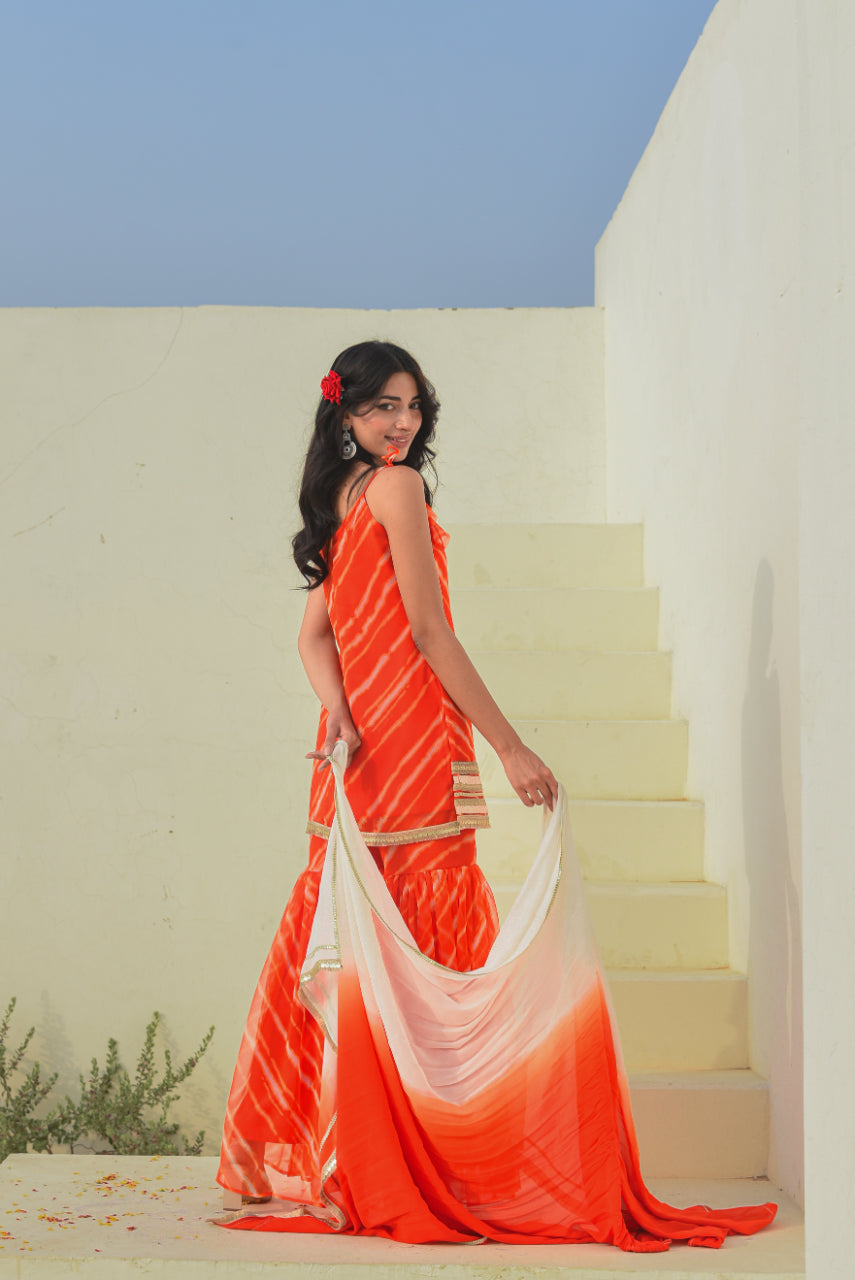 Woman in an orange saree standing on a staircase with a clear blue sky.