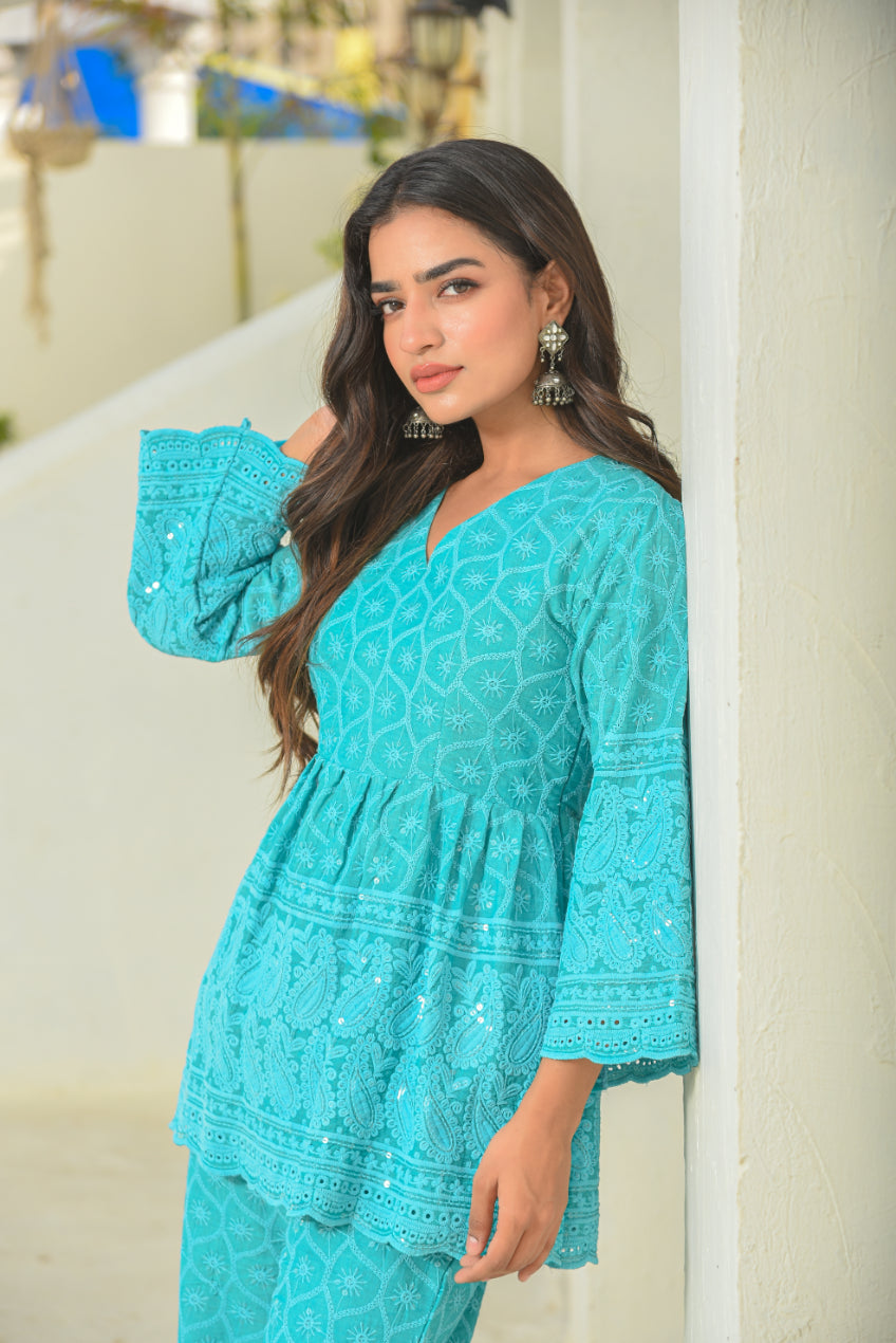 Woman wearing a turquoise lace outfit standing against a white wall.