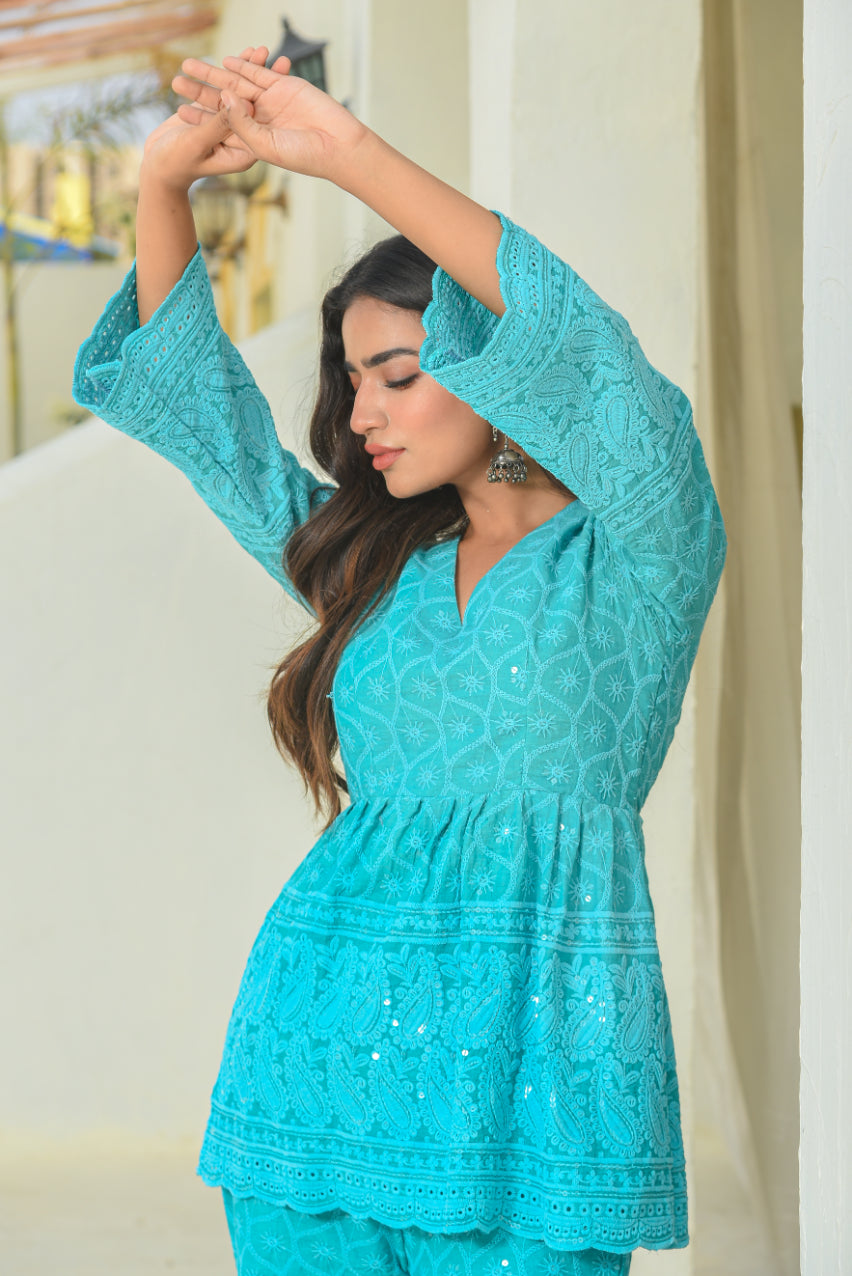 Woman wearing a turquoise embroidered outfit with a neutral background