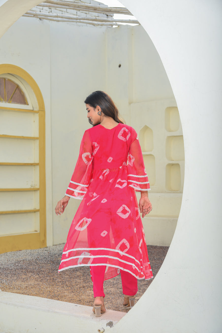 Woman wearing a pink traditional outfit with white patterns in a neutral setting