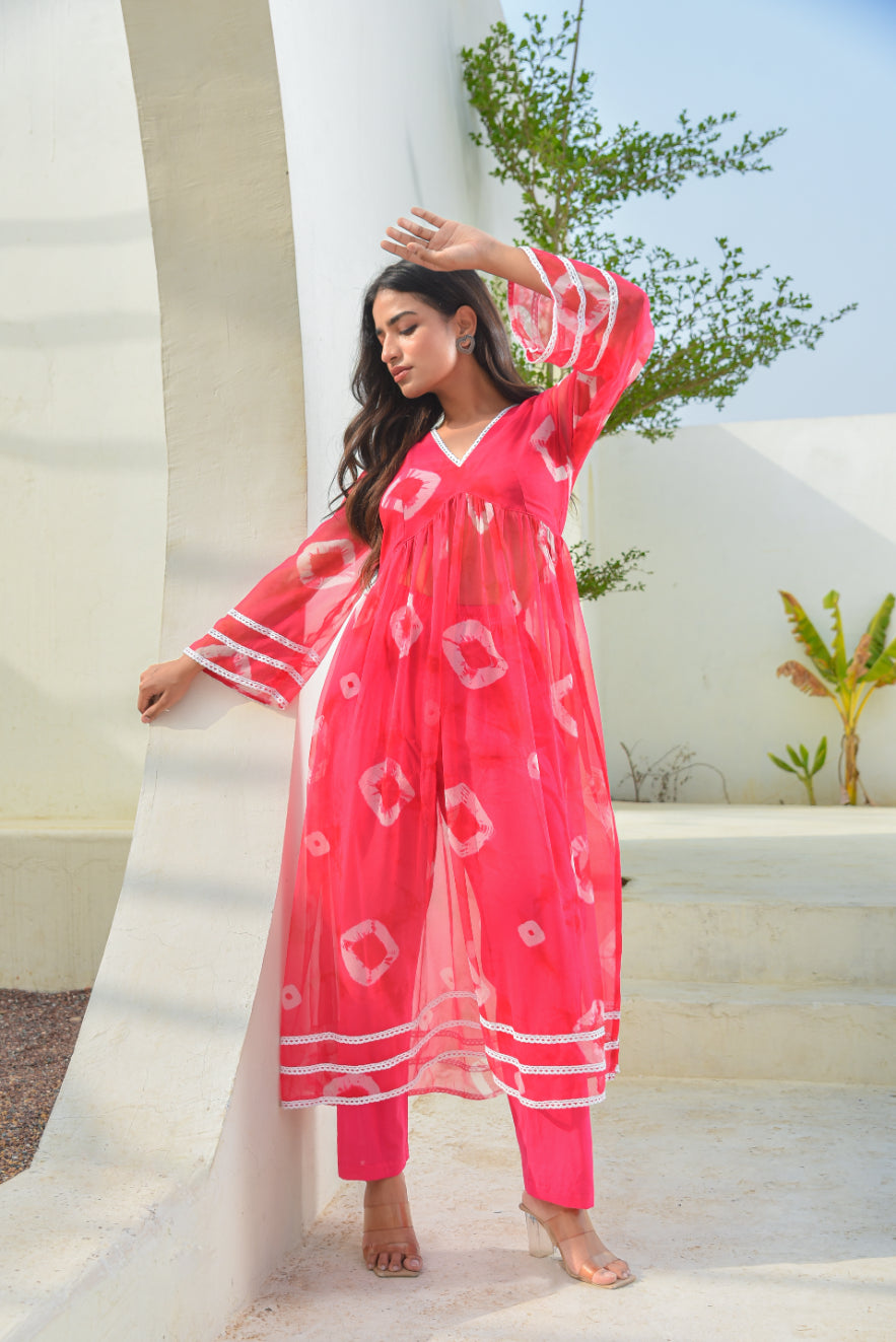 Woman in a pink outfit standing against a white wall with greenery in the background