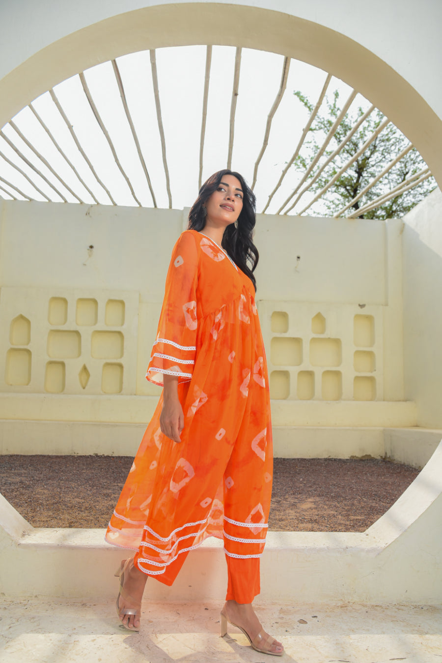 Woman in an orange dress standing in front of a decorative white archway.
