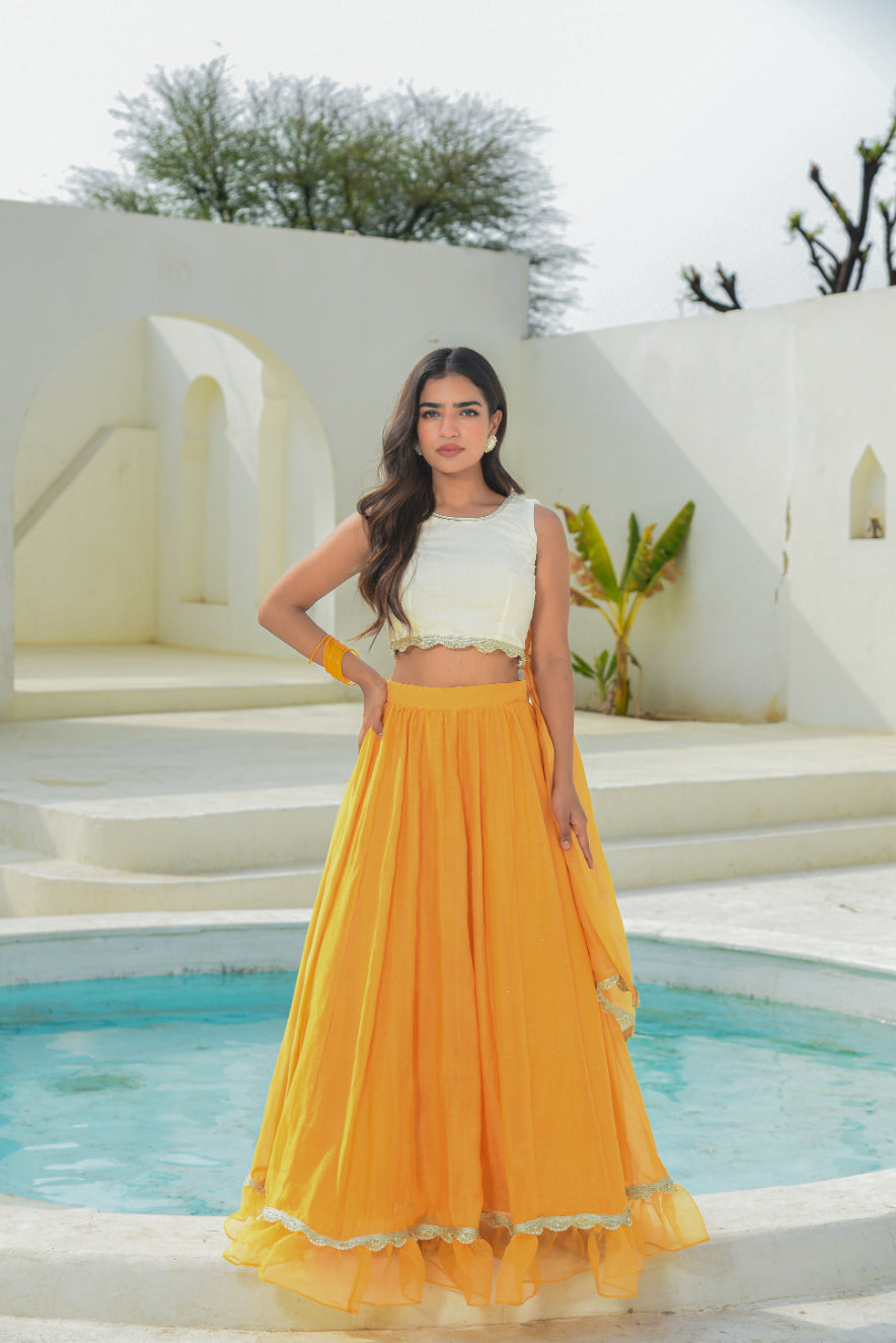 Woman in a white top and yellow skirt standing by a pool with white architecture and greenery in the background